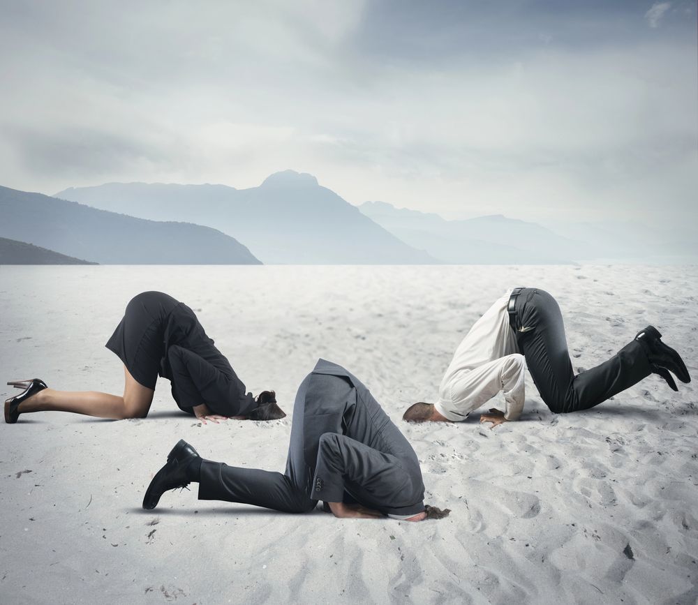 Three people are kneeling in the sand with their heads in the sand