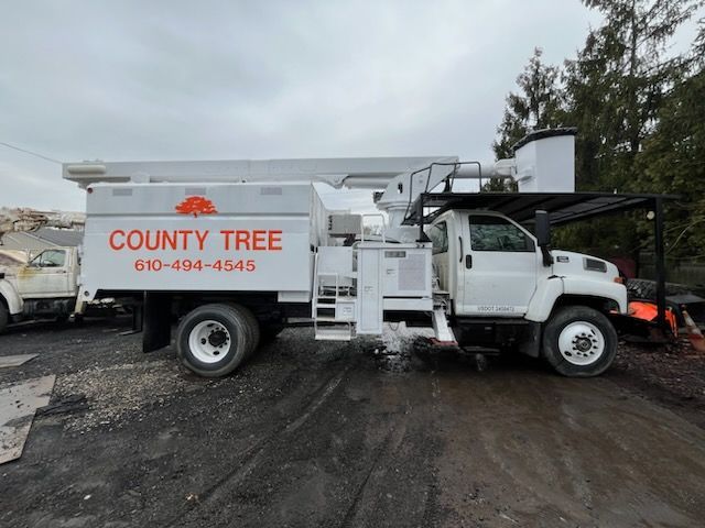 A white county tree truck is parked in a dirt lot