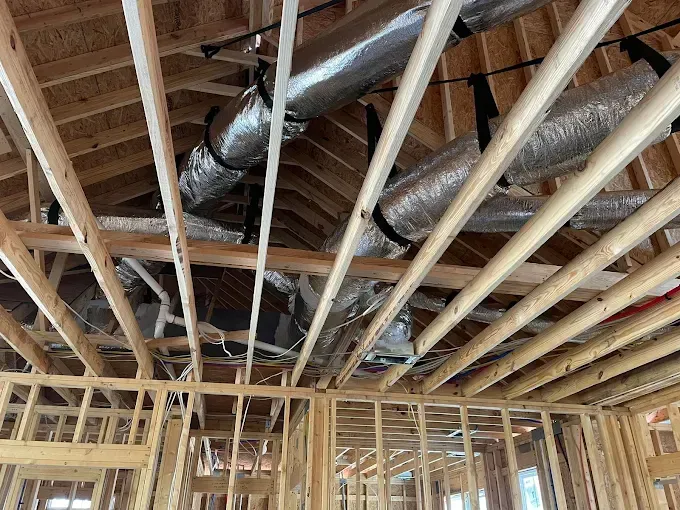 Interior framing of a building under construction, showing wooden beams and HVAC ductwork in the ceiling.