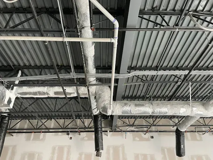 Exposed ceiling with ductwork, pipes, and metal beams in a building under construction.