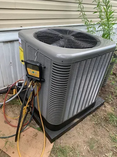 Air conditioning unit being serviced outdoors, with gauges and hoses attached. Gray and black.