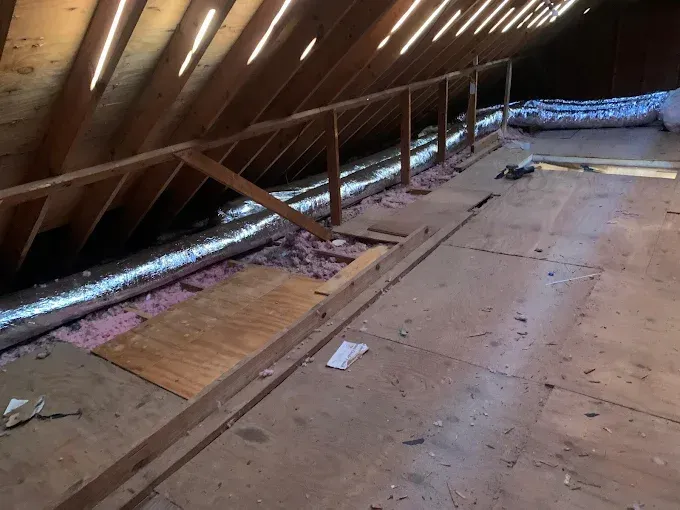 Interior view of an attic with exposed wooden beams, insulation, and a safety railing.