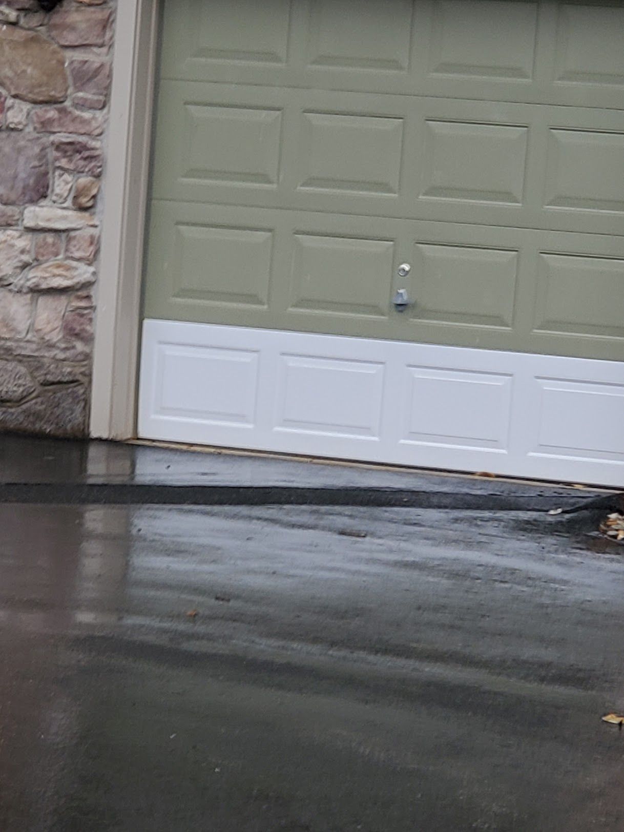 A green garage door with a white trim is next to a stone wall.