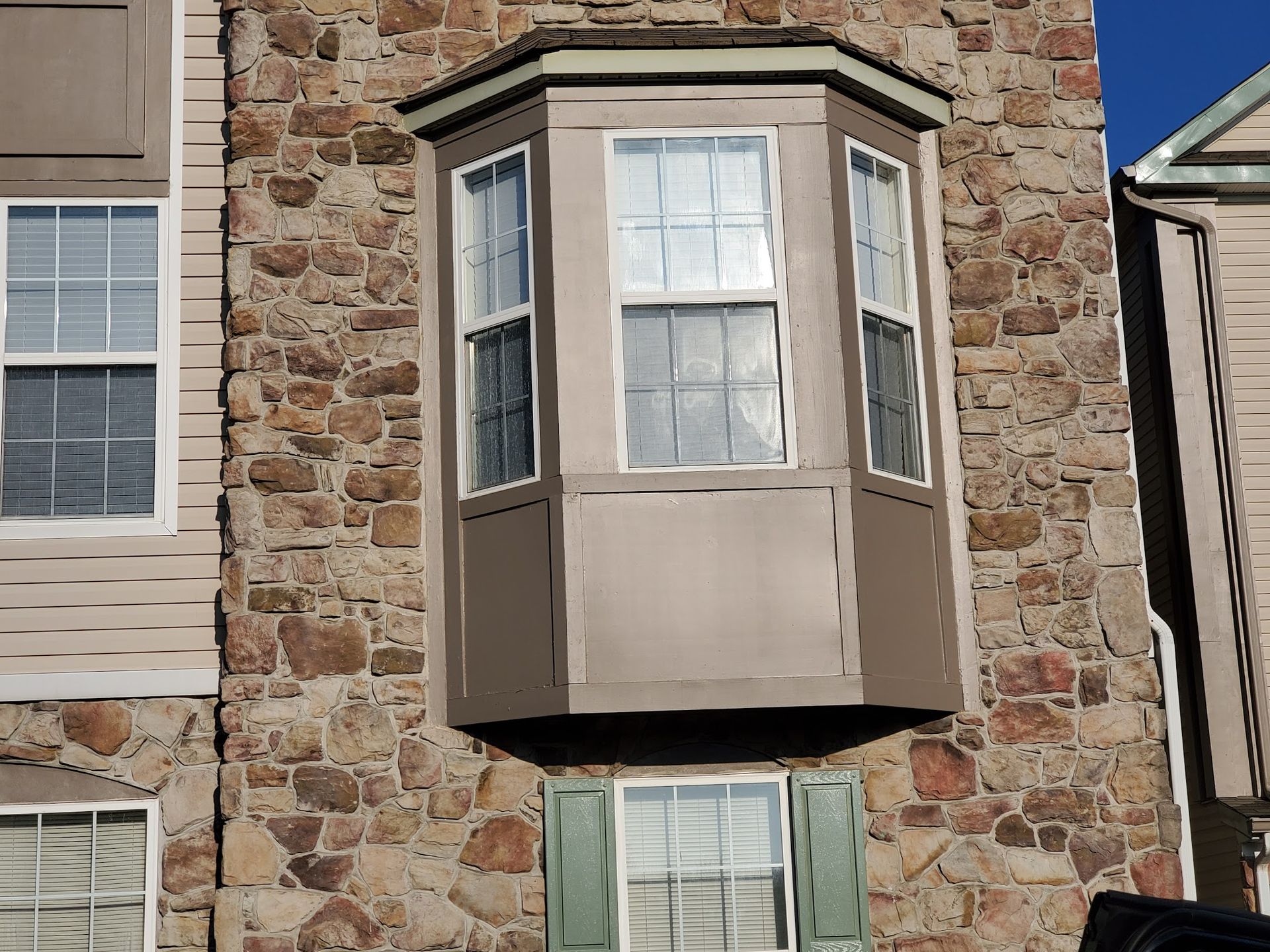 A stone building with a bay window and green shutters