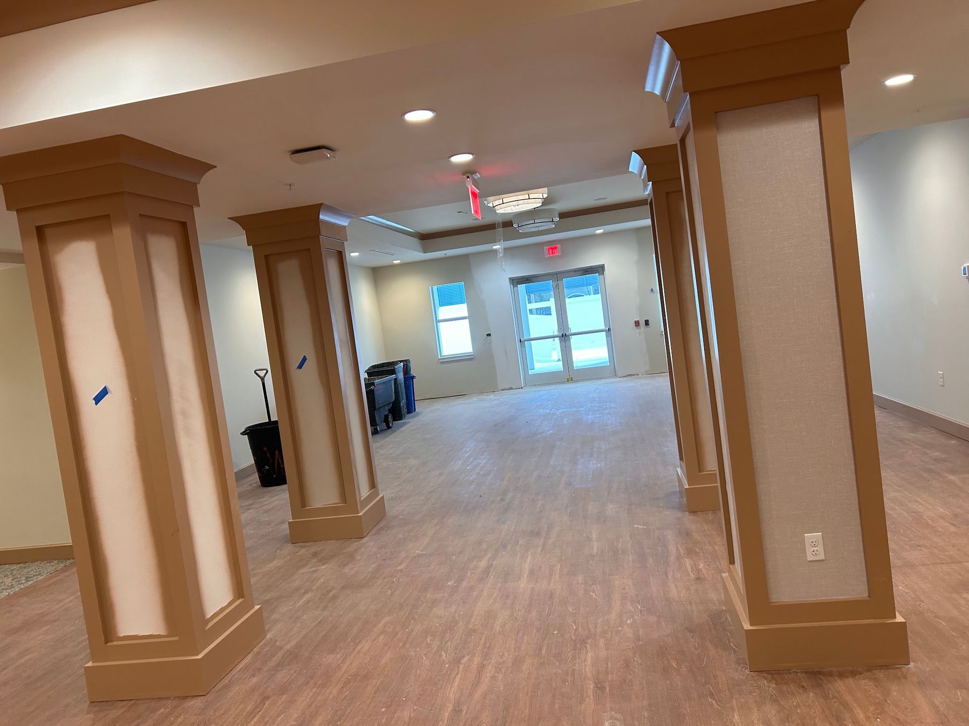 A large empty room with columns and a red exit sign.
