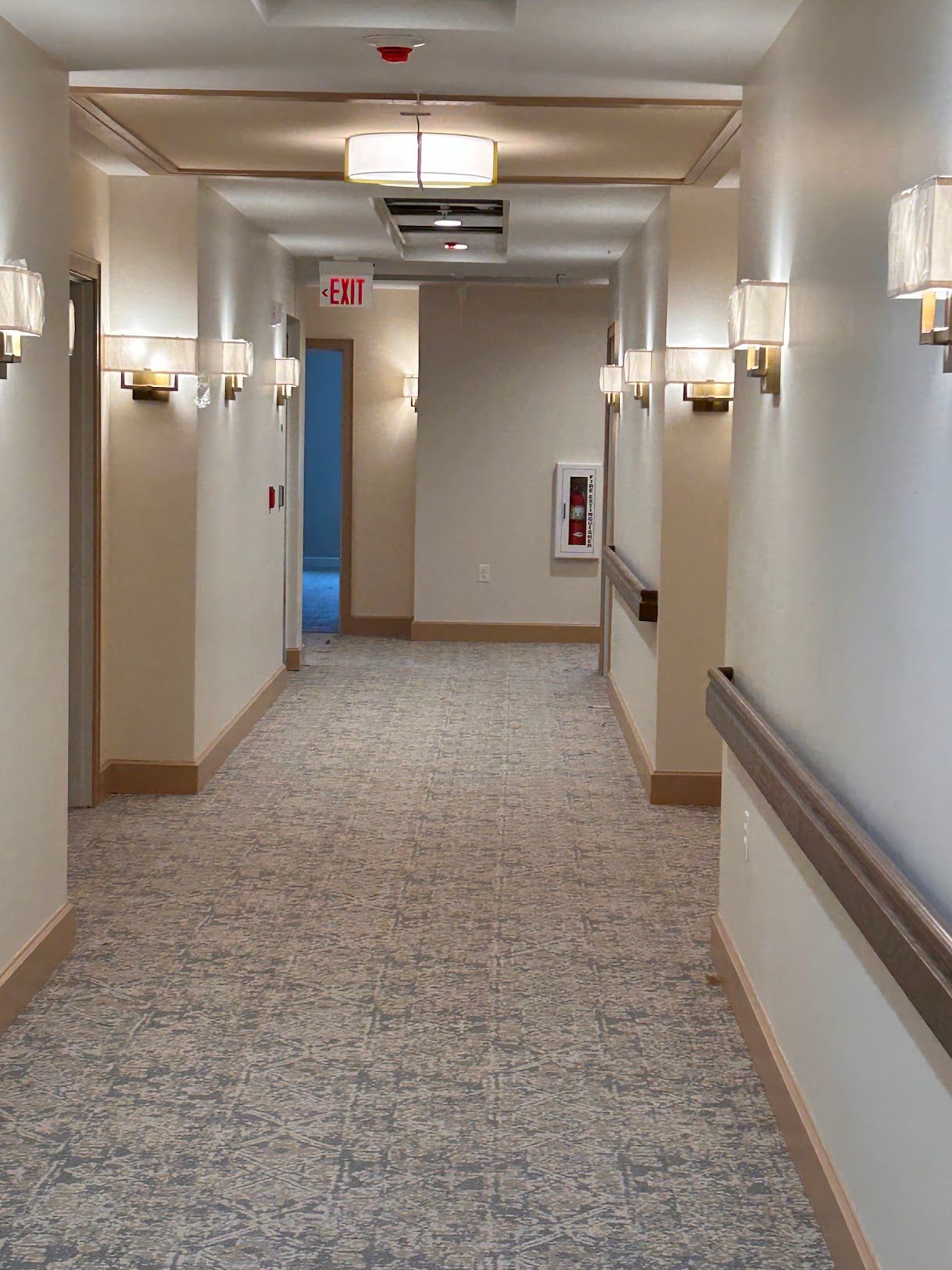 A long hallway with a carpeted floor and a fire extinguisher on the wall.