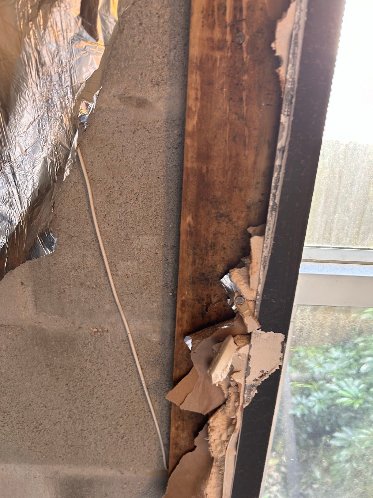 A piece of wood is missing from a wall next to a window.