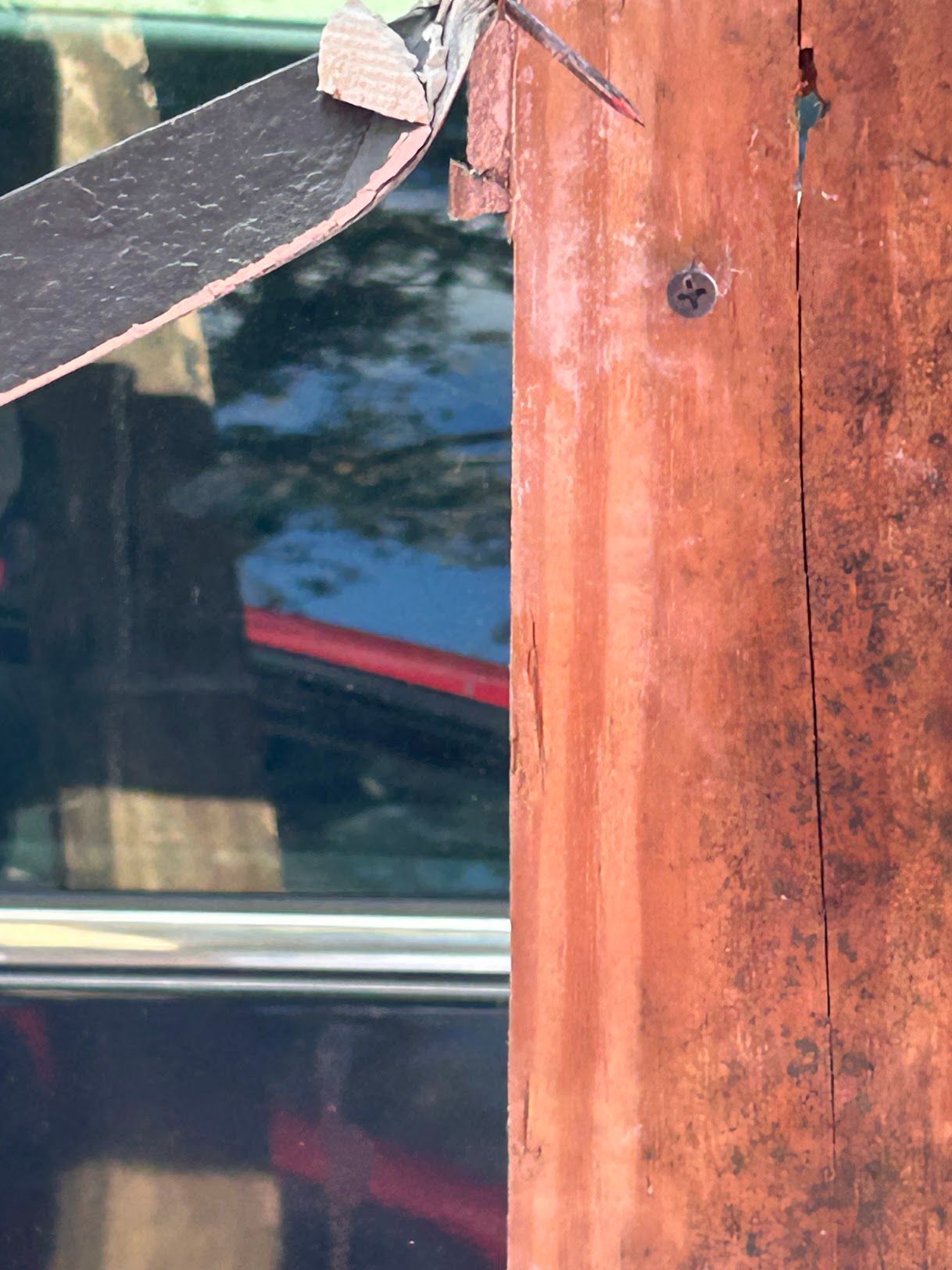 A bug is sitting on a wooden post next to a window.