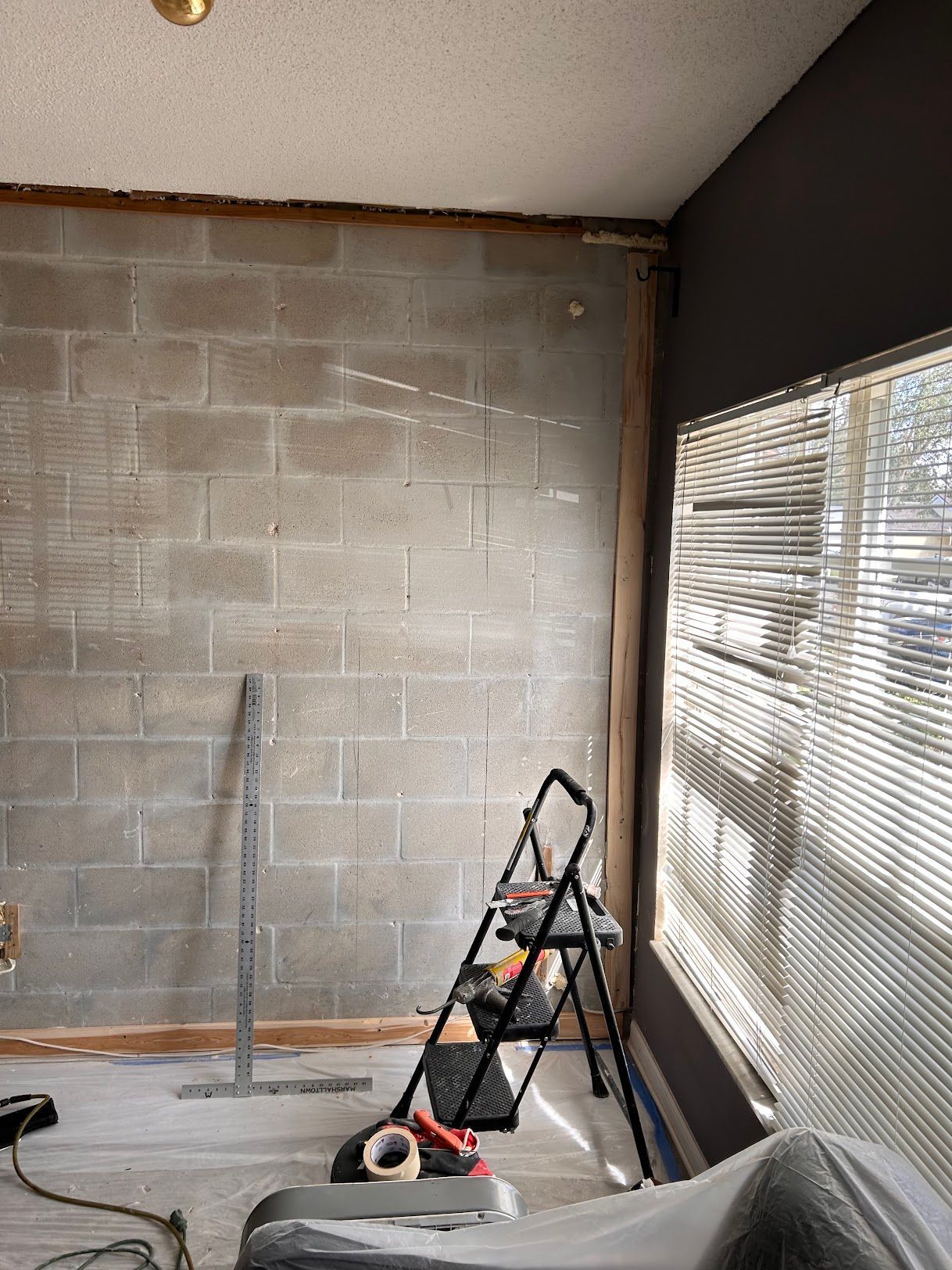 A room with a ladder and a window with blinds.