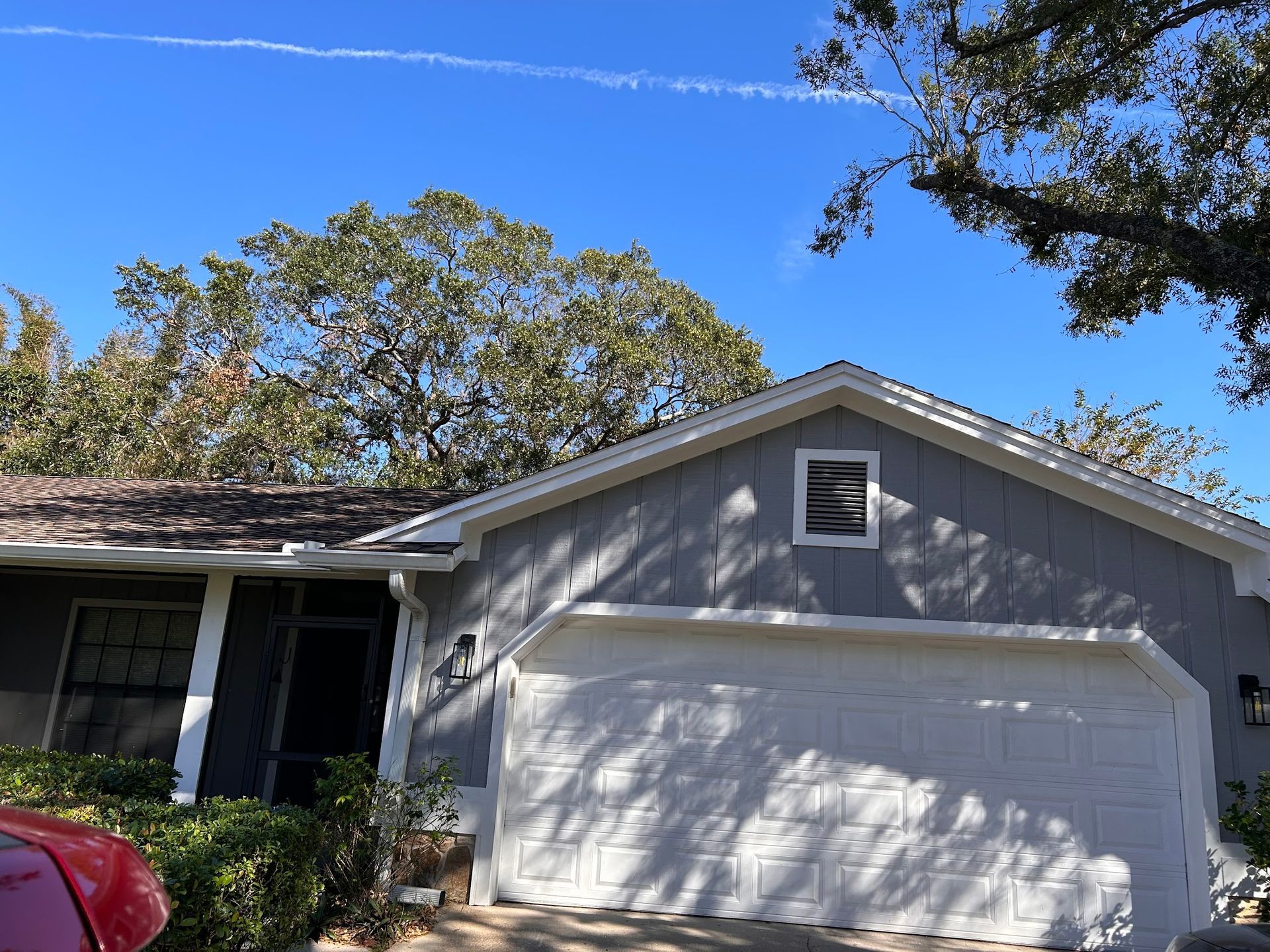 A gray house with a white garage door and a red car parked in front of it.