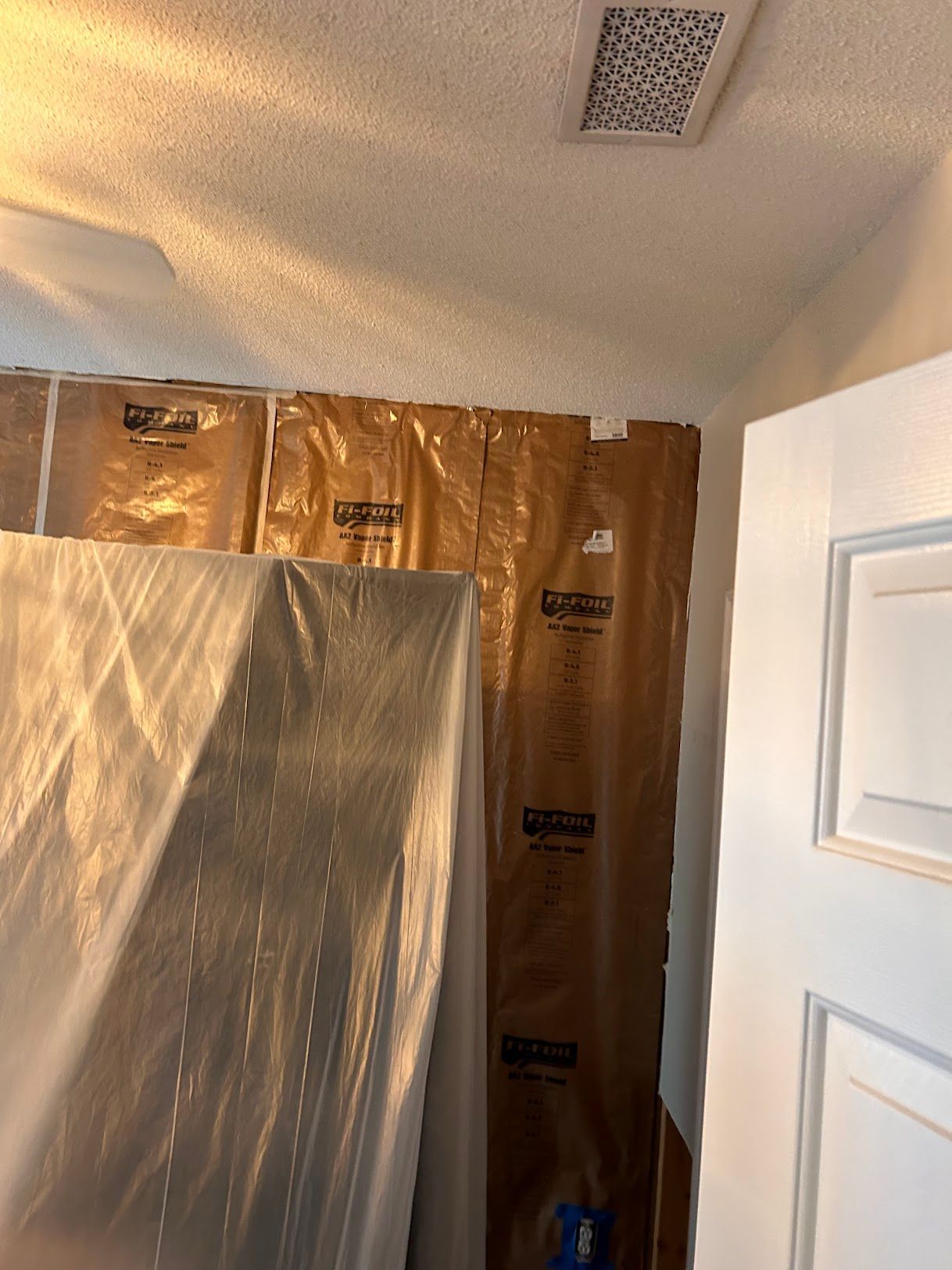 A room with a ceiling fan and a plastic sheet on the wall.