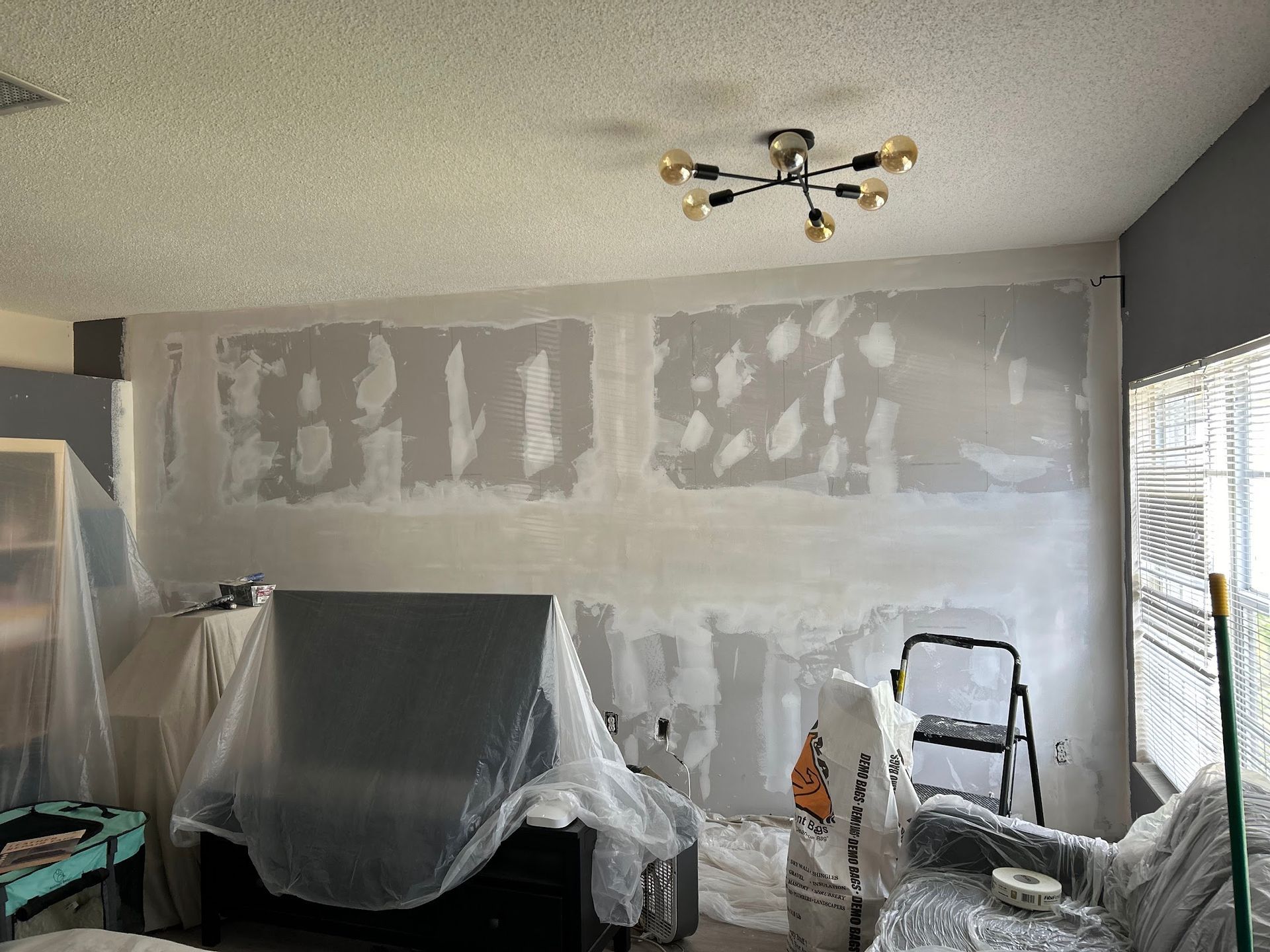 A living room with a couch covered in plastic and a ladder.