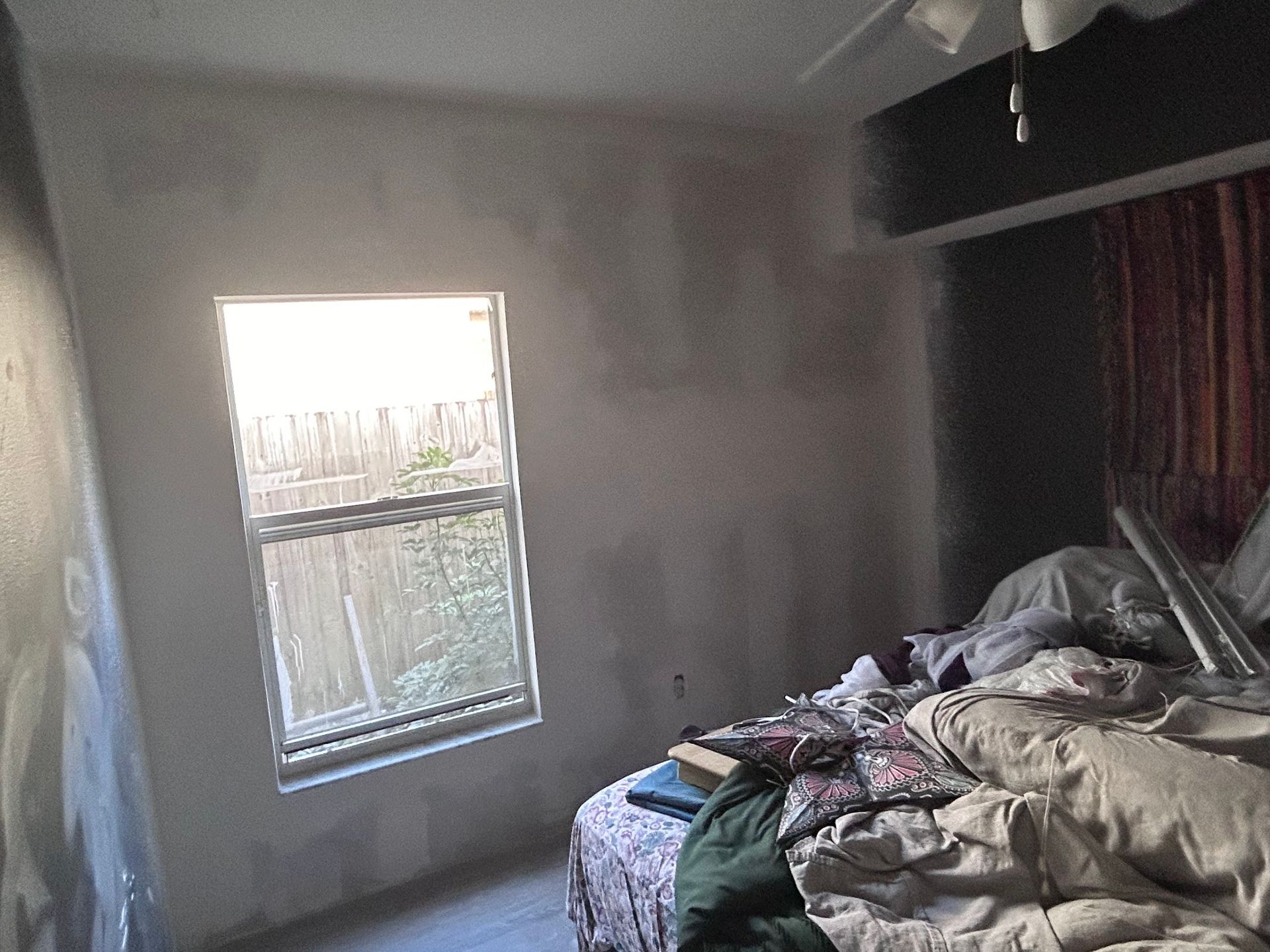 A bedroom with a bed and a window with a ceiling fan.