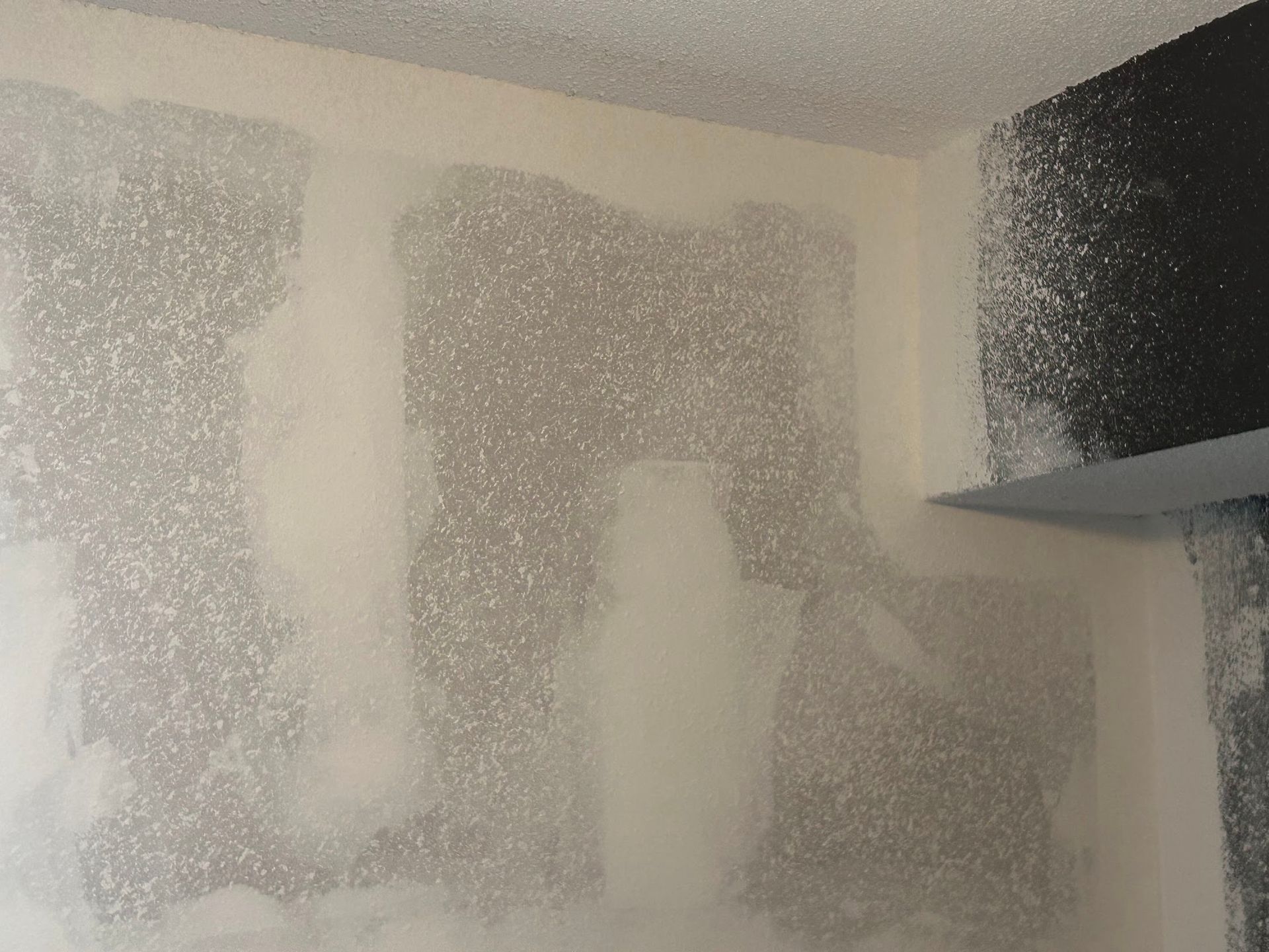 A white wall with a few spots of black paint on it