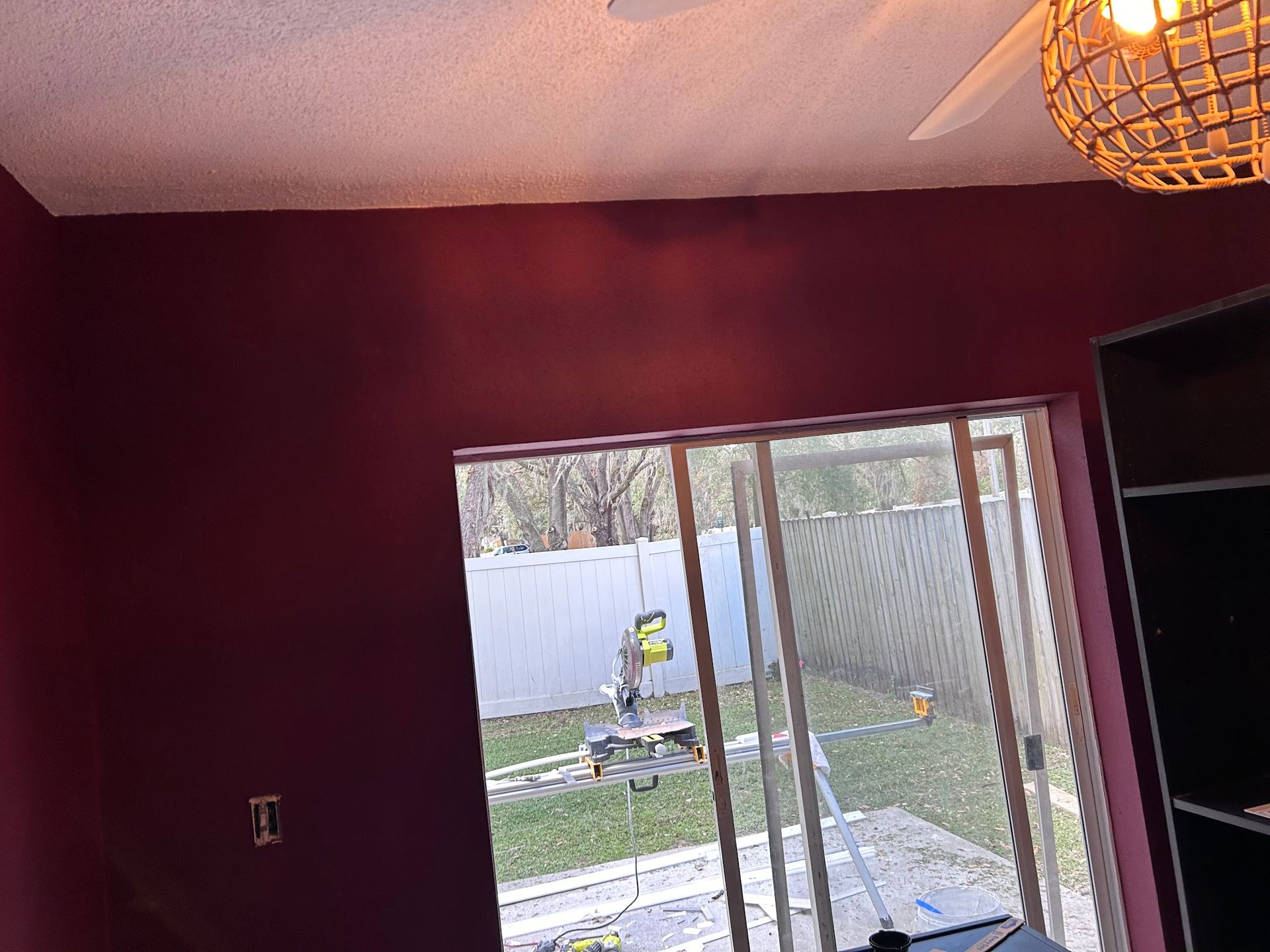 A room with red walls and a large window with a ceiling fan.