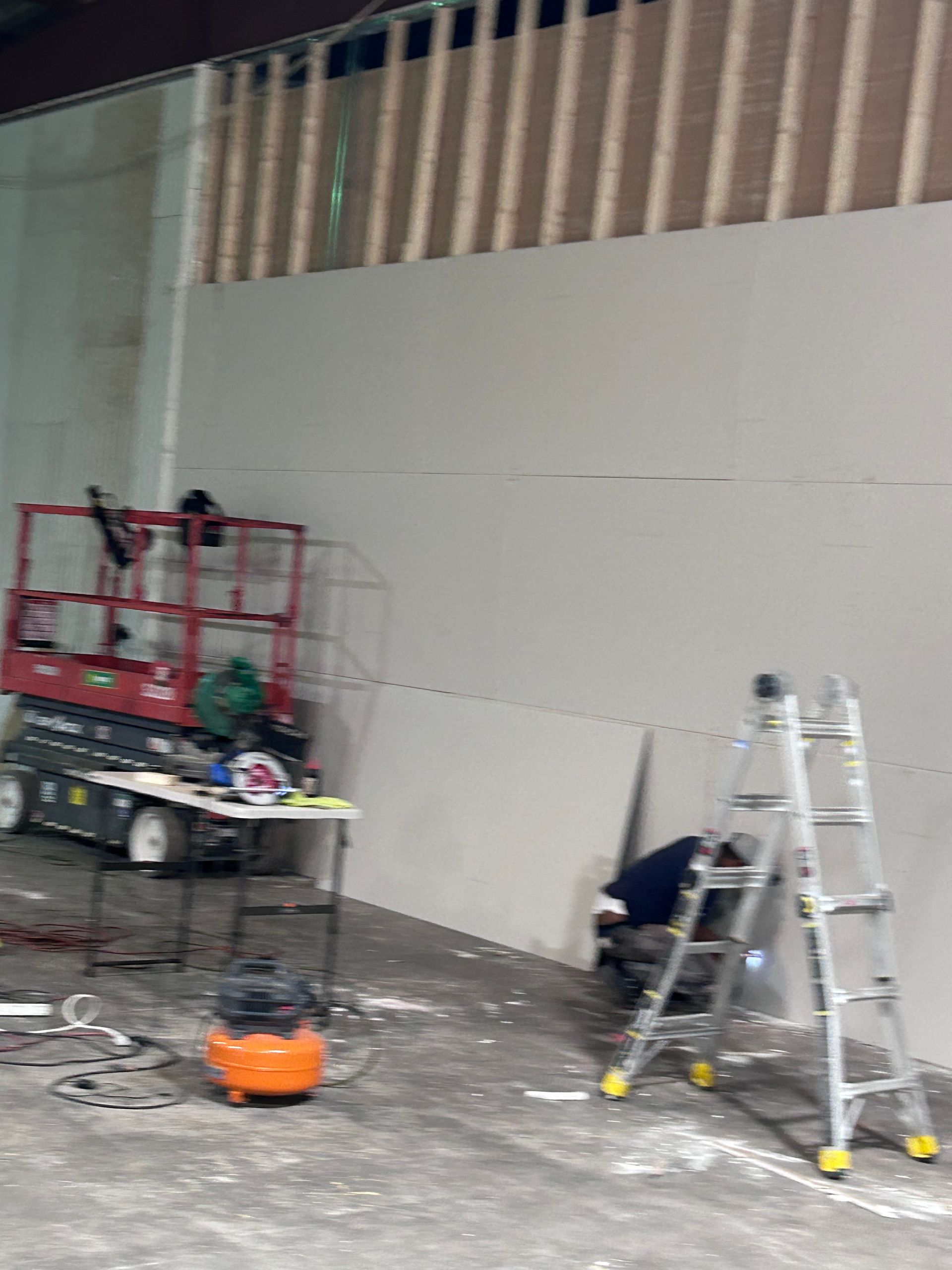 A man is working on a wall in a warehouse with a ladder.