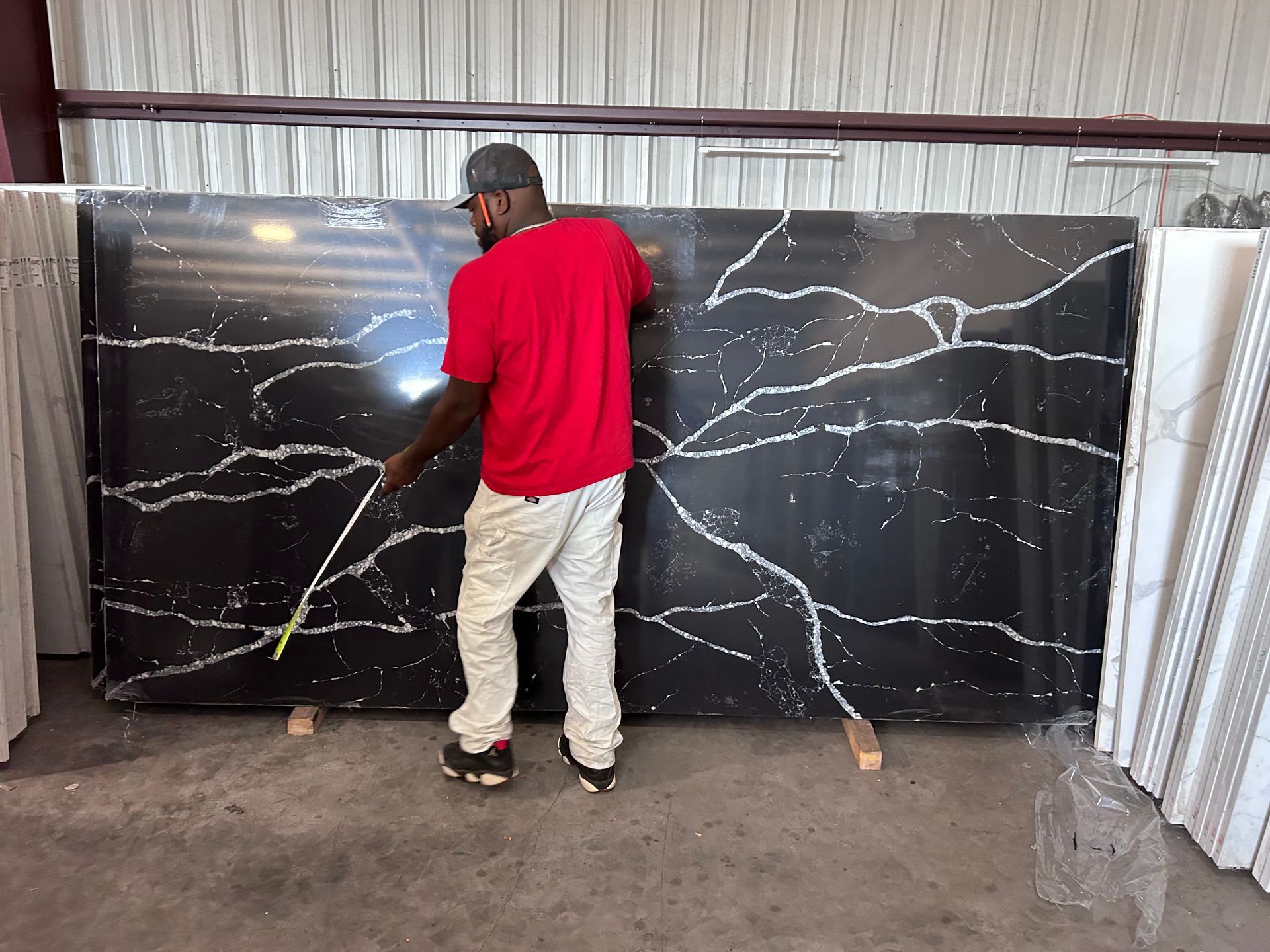 A man in a red shirt is measuring a large black stone slab