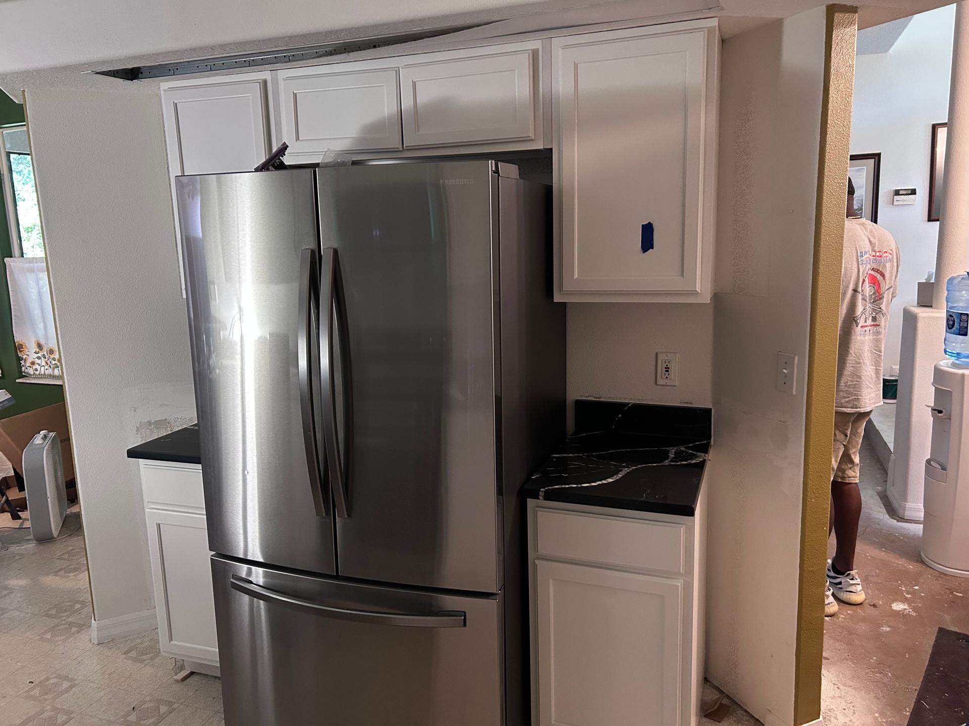 A stainless steel refrigerator is in a kitchen with white cabinets.