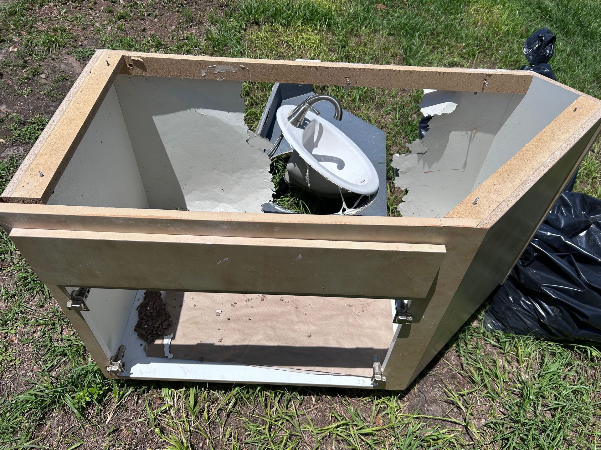 A broken cabinet is sitting on the grass next to a black bag