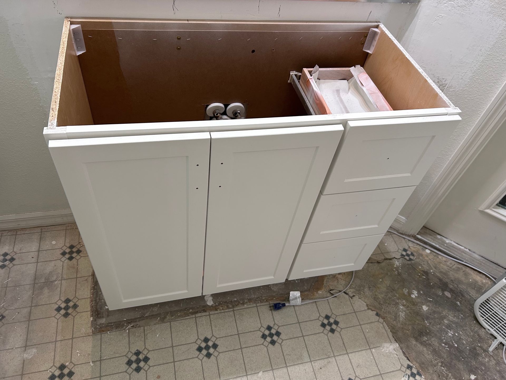 A white cabinet is sitting on a tiled floor.
