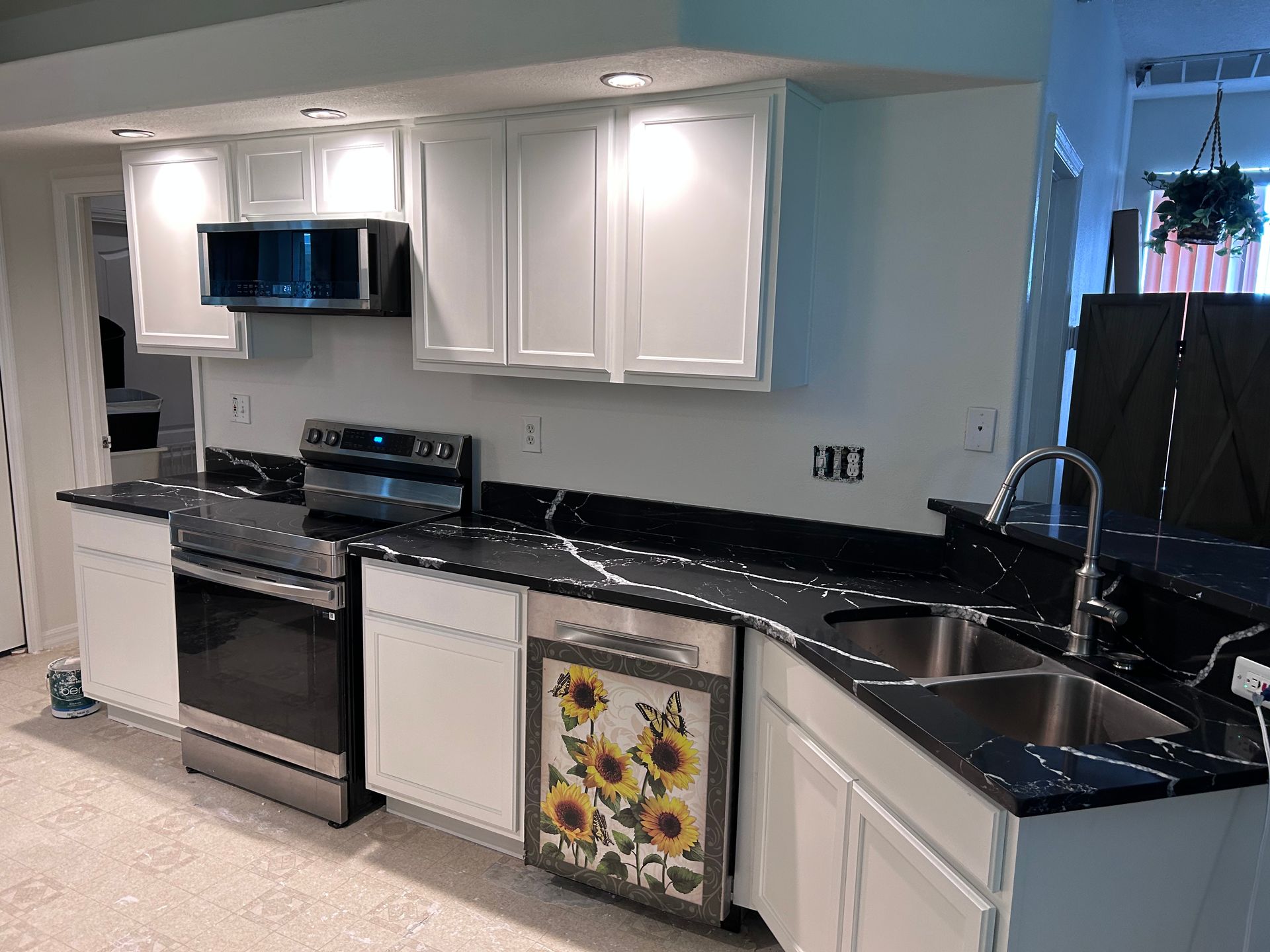 A kitchen with black counter tops , white cabinets , stainless steel appliances , and a sunflower dishwasher.