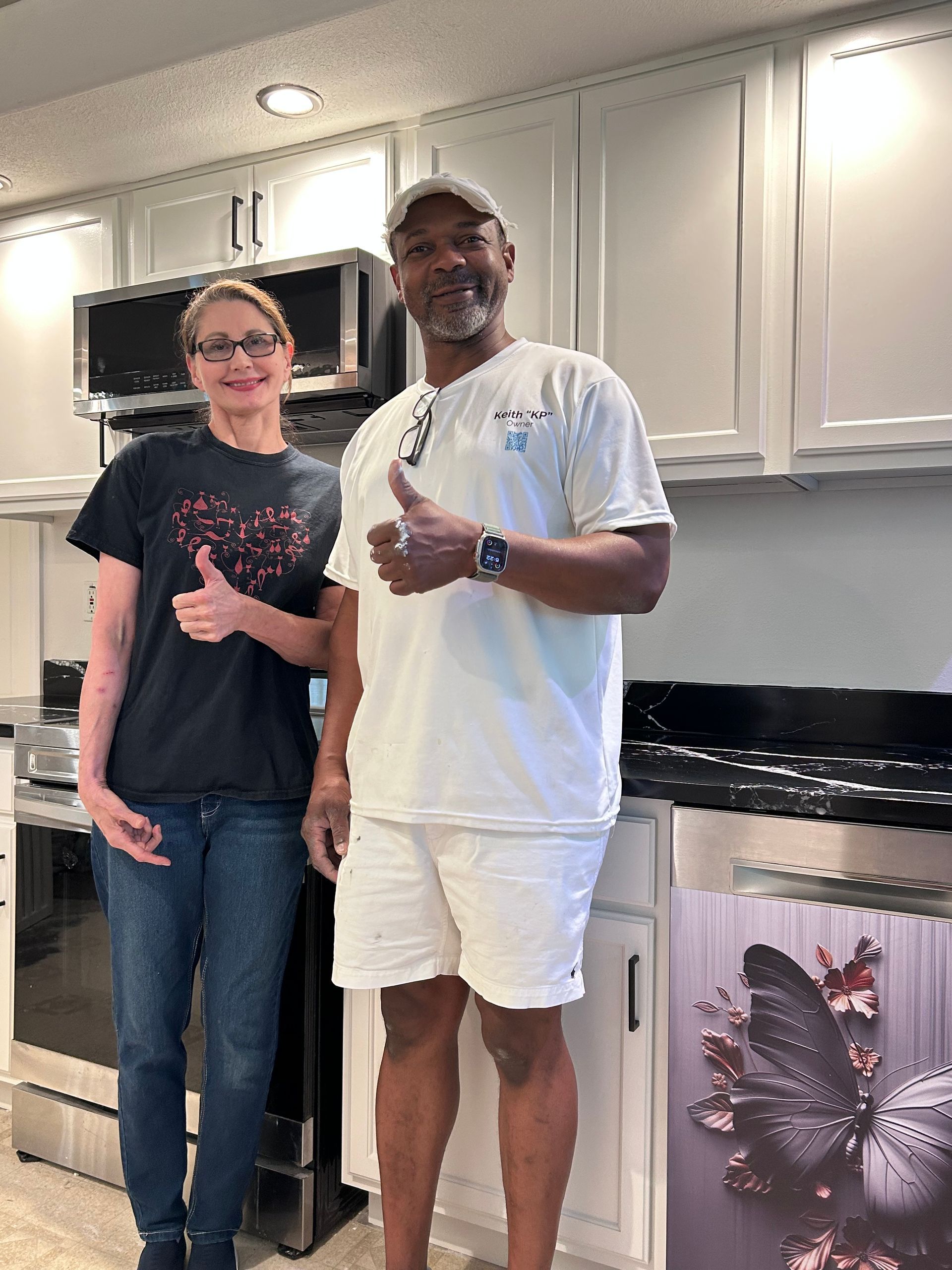 A man and a woman are standing in a kitchen giving a thumbs up.