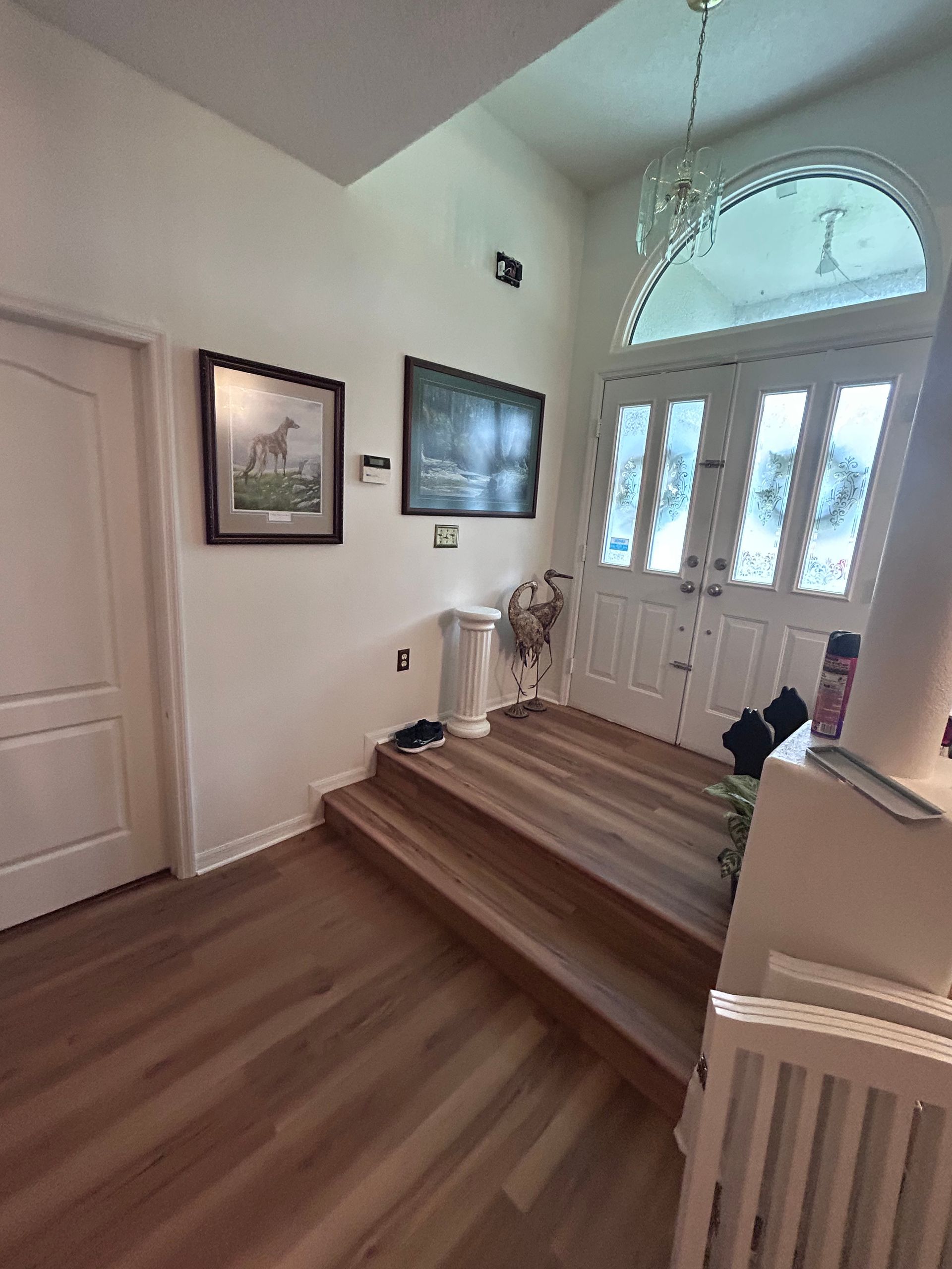 A hallway with stairs leading up to a door and a picture on the wall.