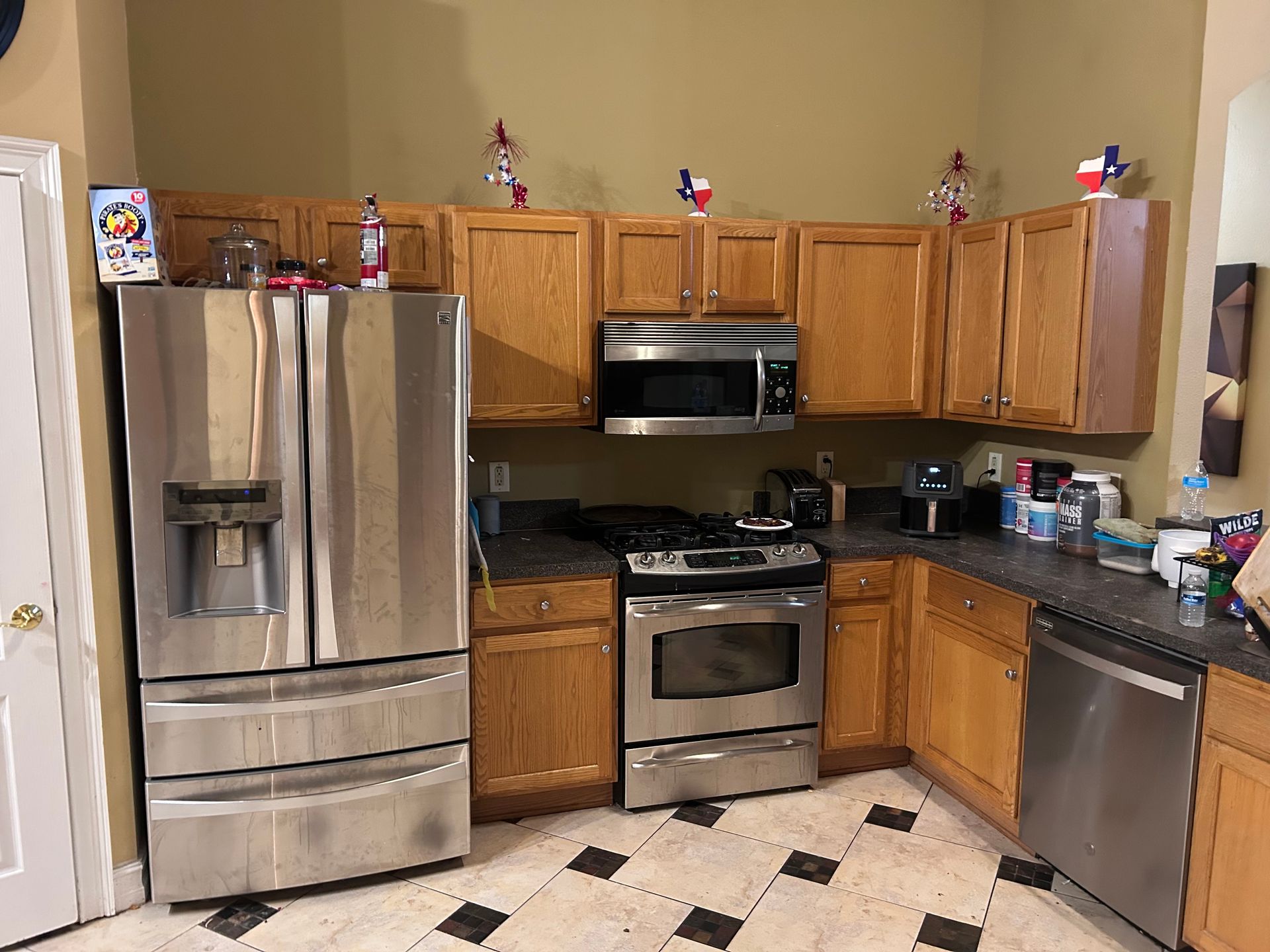 Kitchen with stainless steel appliances, oak cabinets, dark countertops, and tile floor; Texas-themed decorations.