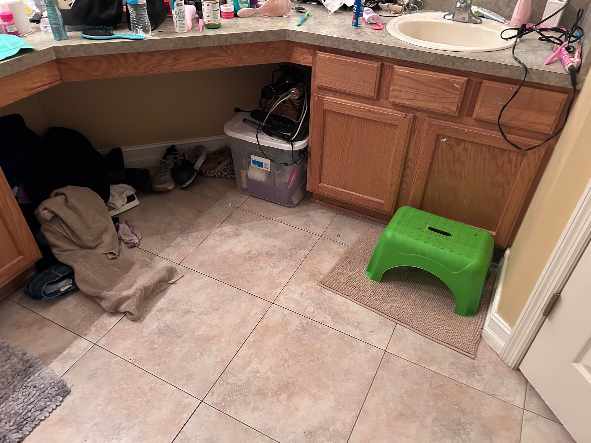 Bathroom with cluttered countertop, cabinets, and a green step stool on a small rug.