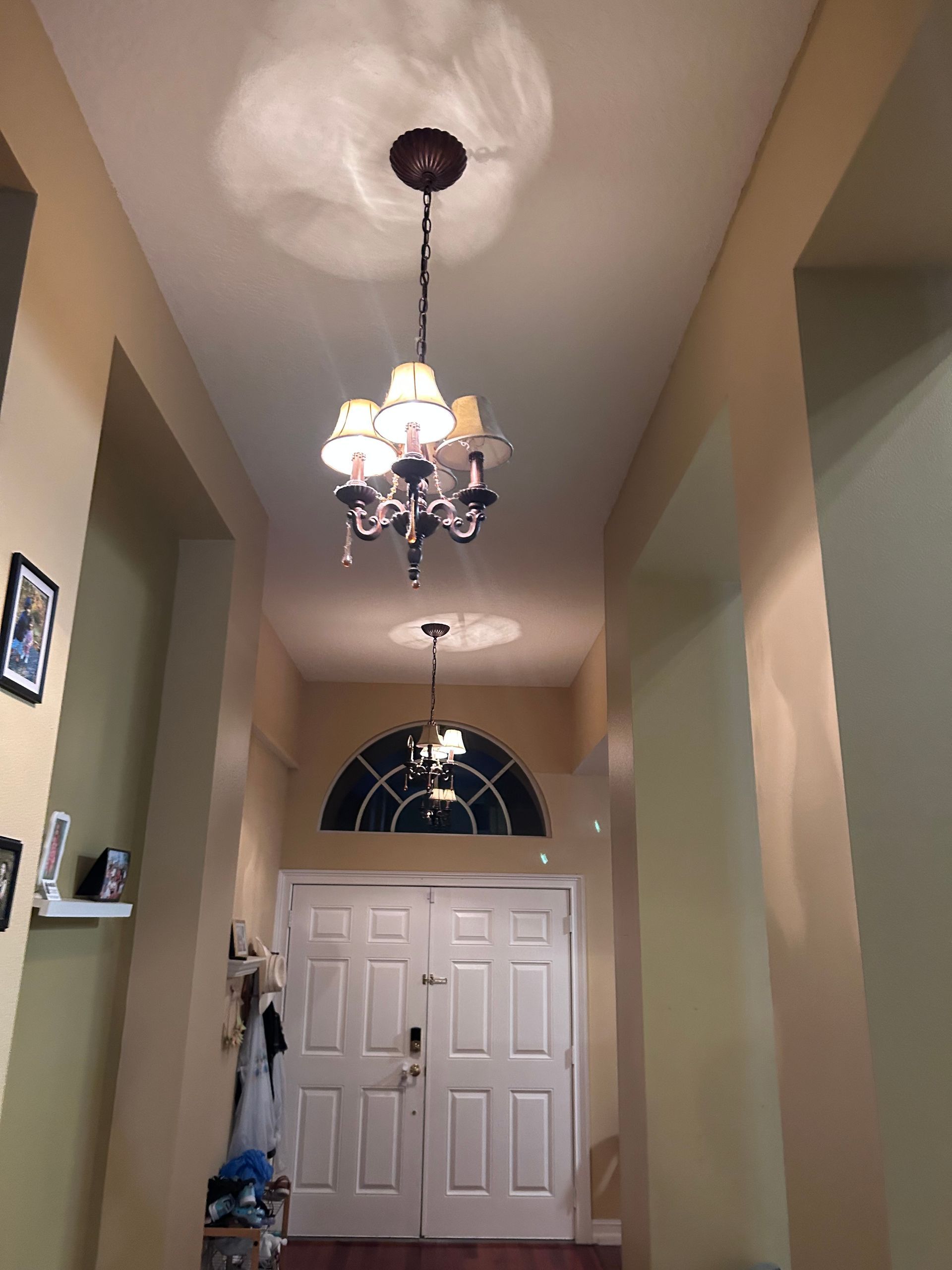 Hallway with two chandeliers, arched doorway, and double doors. Walls are beige.