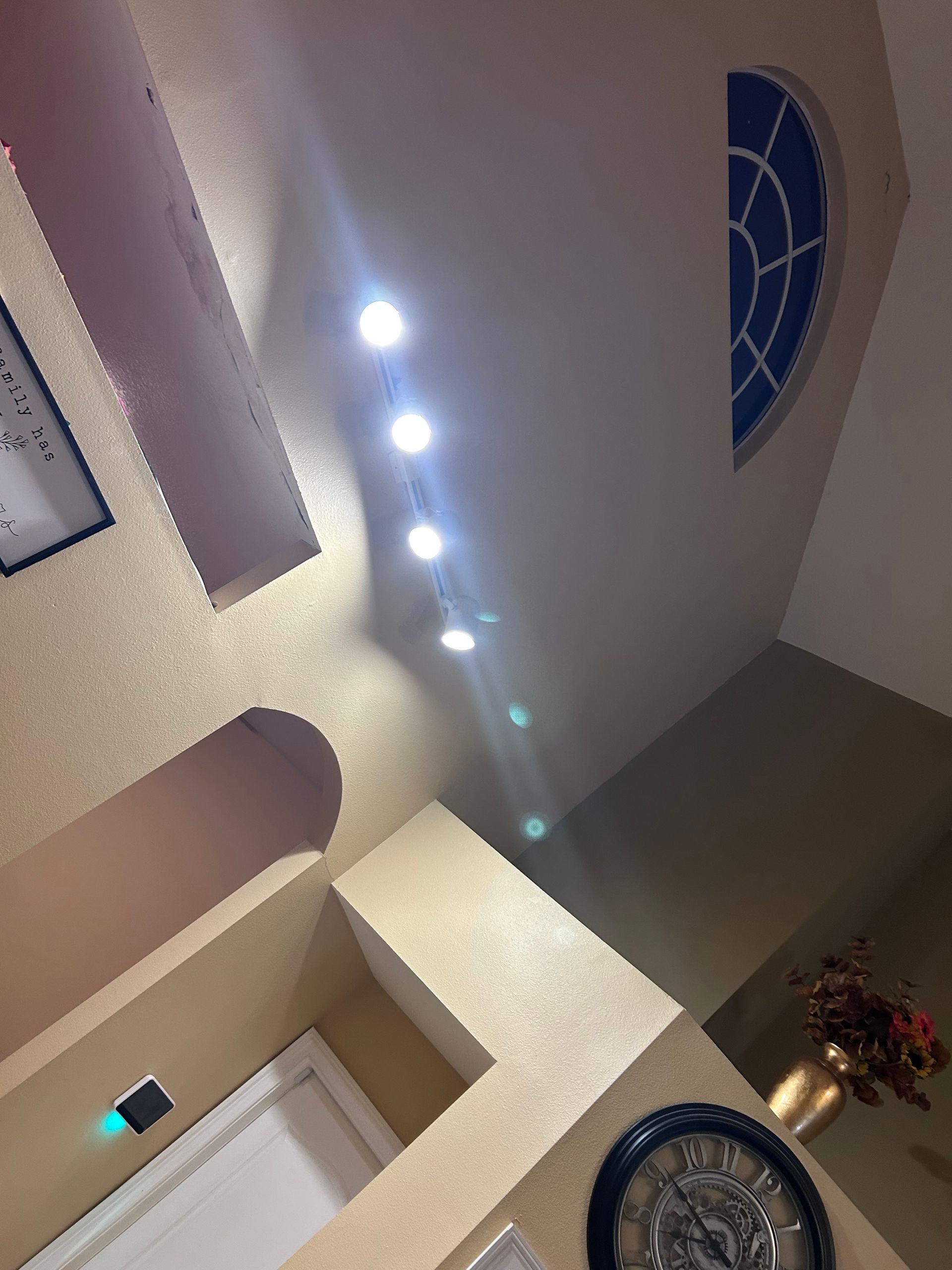 A tall room with recessed lights and arched window. Cream walls and dark clock.