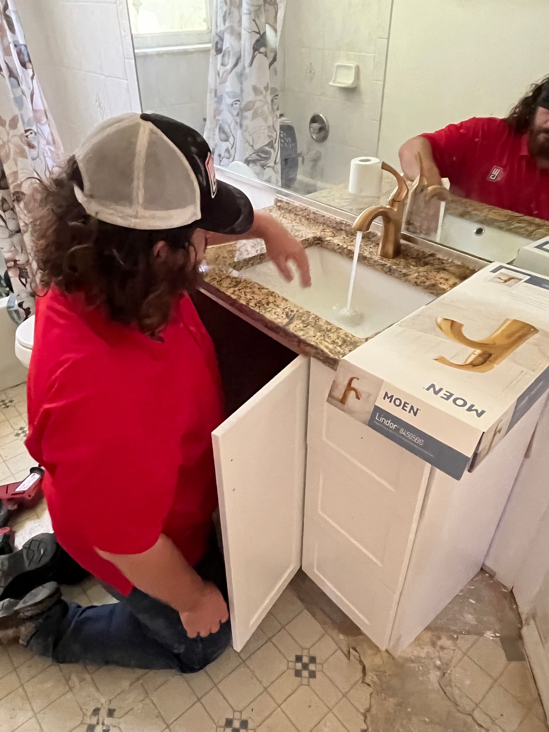 A man is kneeling down in front of a sink in a bathroom.