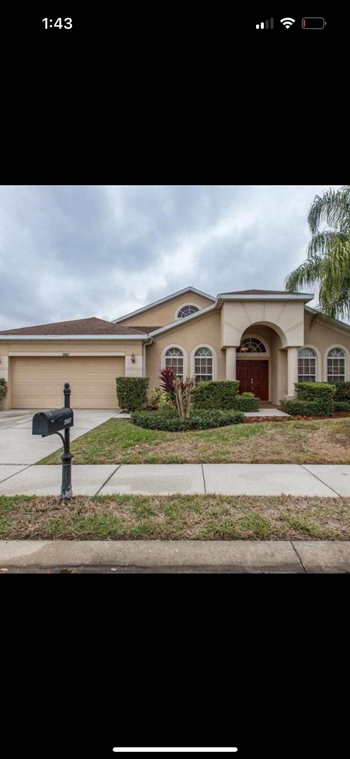 A beige house with a mailbox, driveway, and front lawn under a cloudy sky.