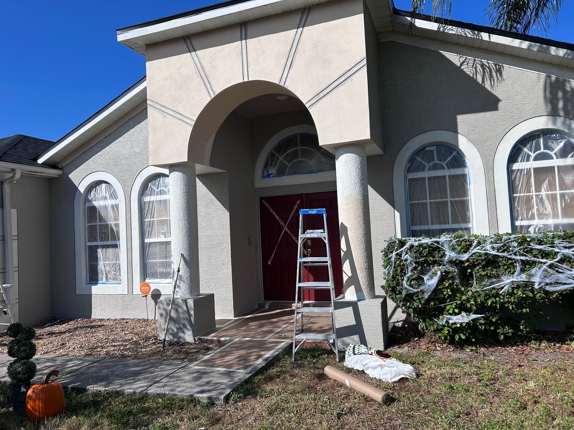A house entrance decorated for Halloween with a red door, archway, and a ladder.