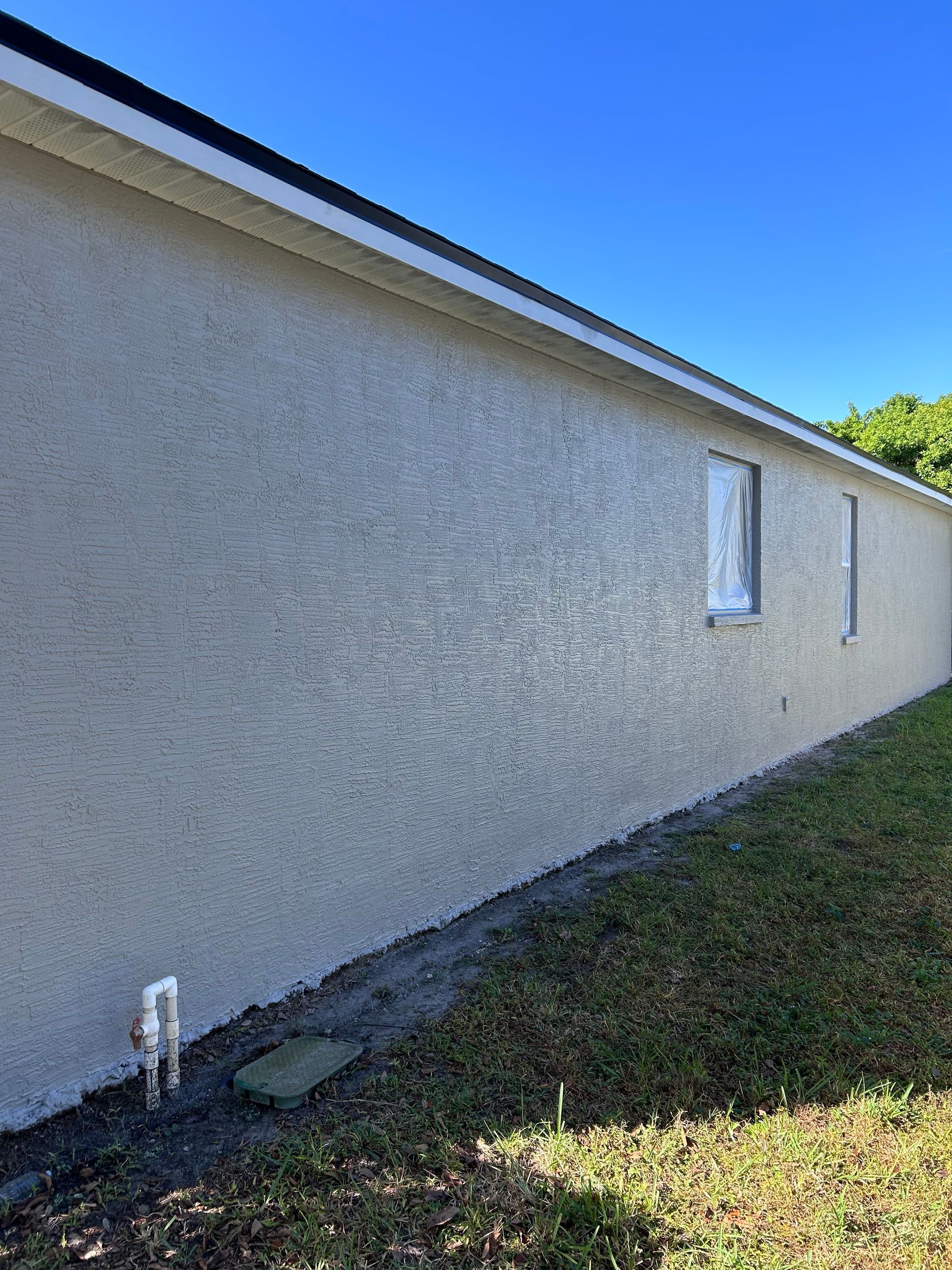 Beige stucco house exterior with two windows, clear blue sky, green grass.