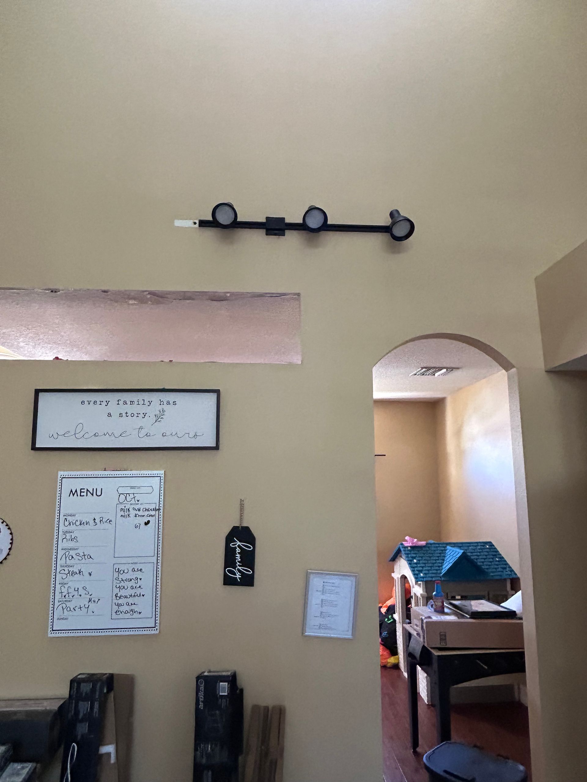 Black track lighting fixture with three lights mounted on a beige wall above a doorway.