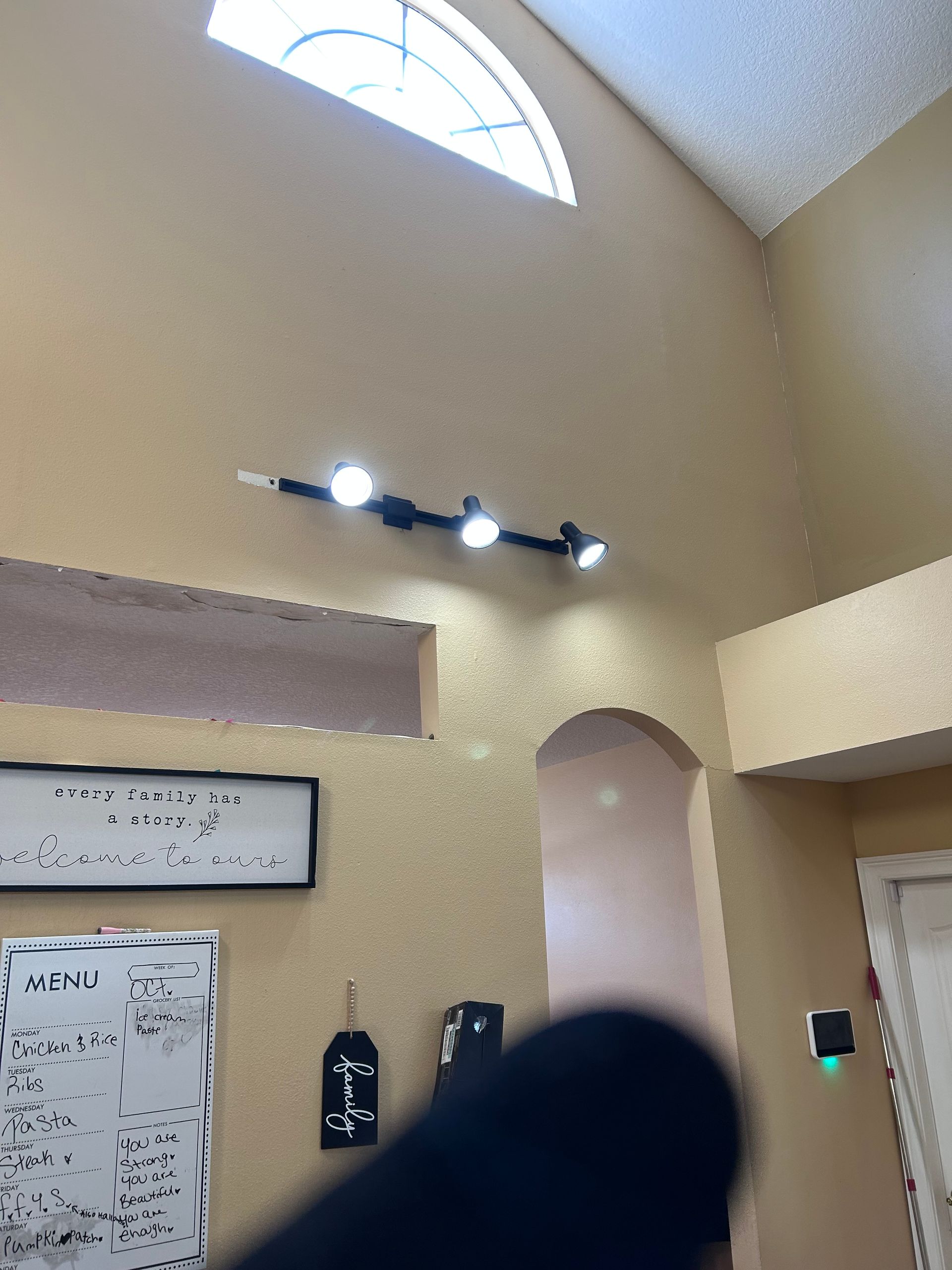 High-ceiling room with track lighting, an arched doorway, and a partially visible window. Beige walls.