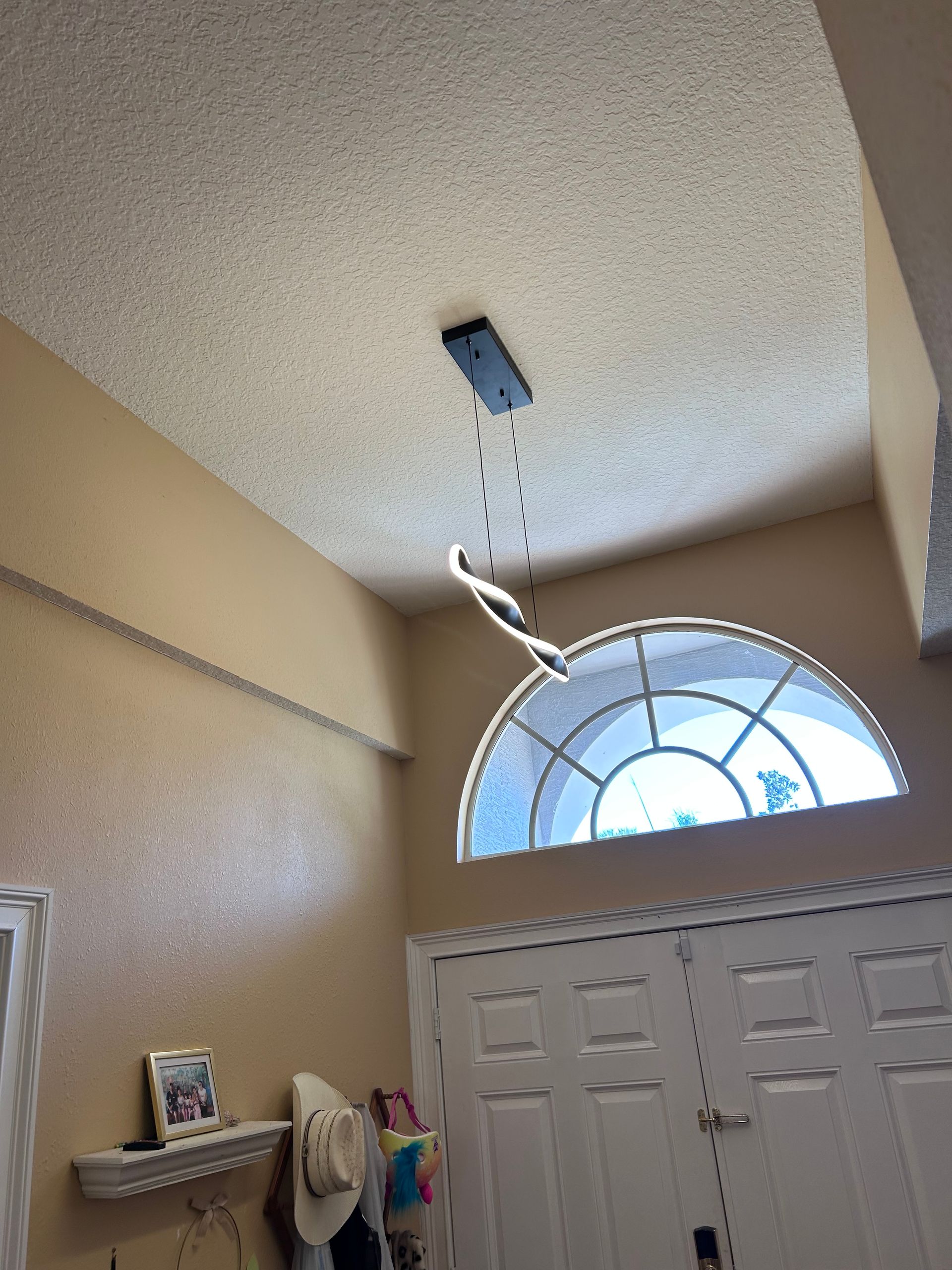 Entryway with a modern light fixture and arched window above white double doors. Beige walls and popcorn ceiling.