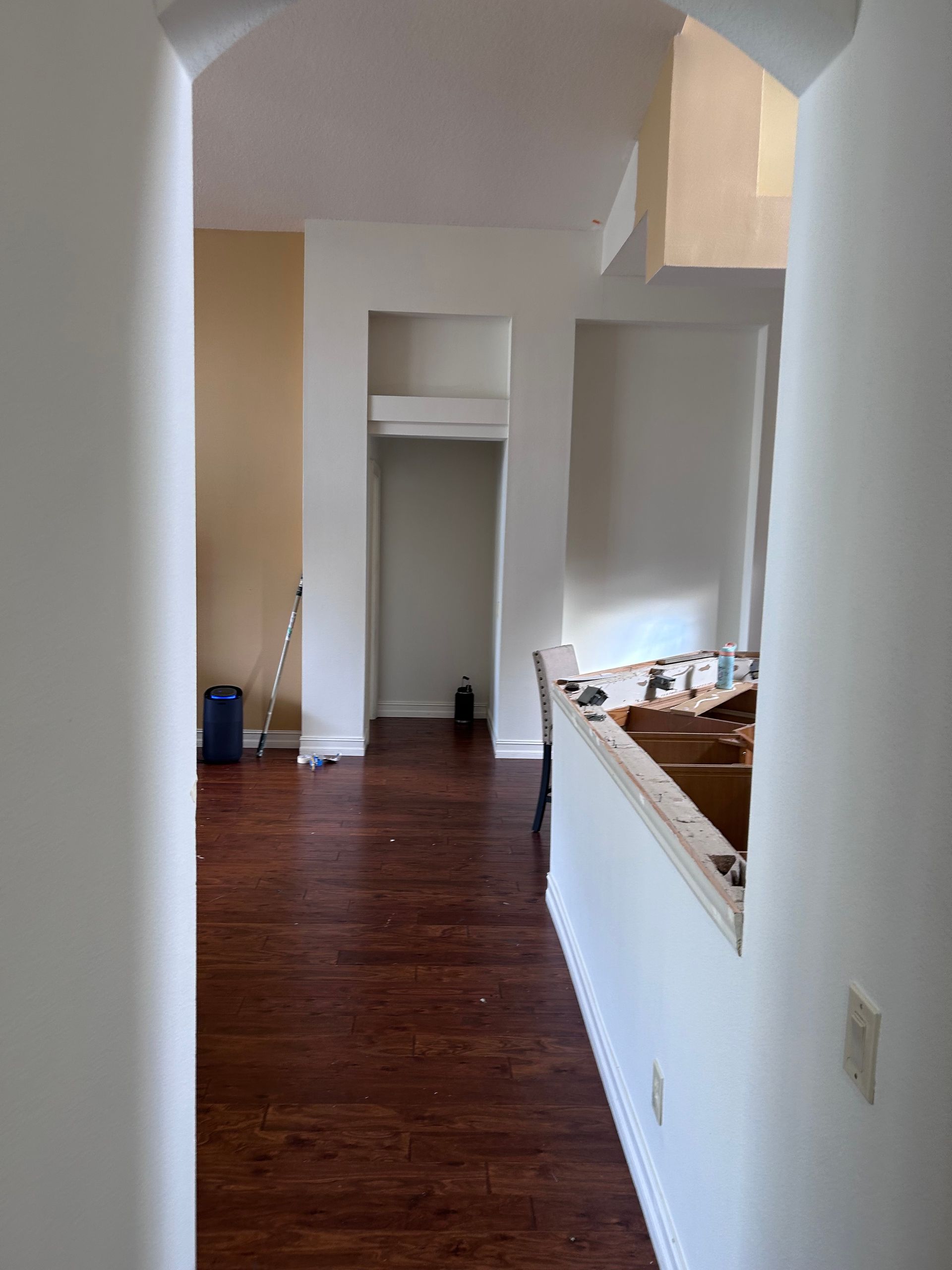 Interior hallway with dark wood flooring, arched doorway, and partial view of a kitchen area.