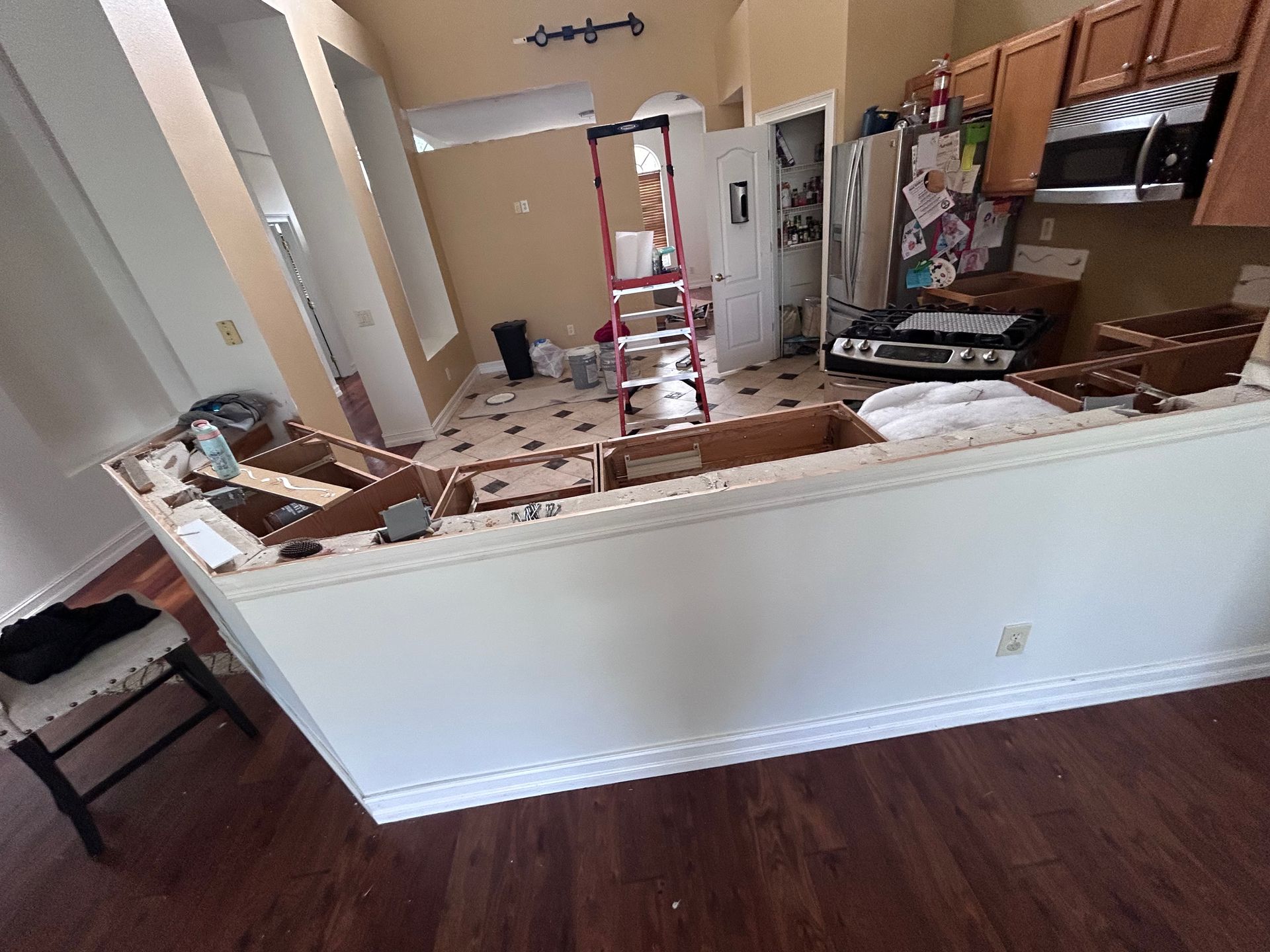 Kitchen renovation with countertop removed, tools, ladder, and partially exposed cabinetry.