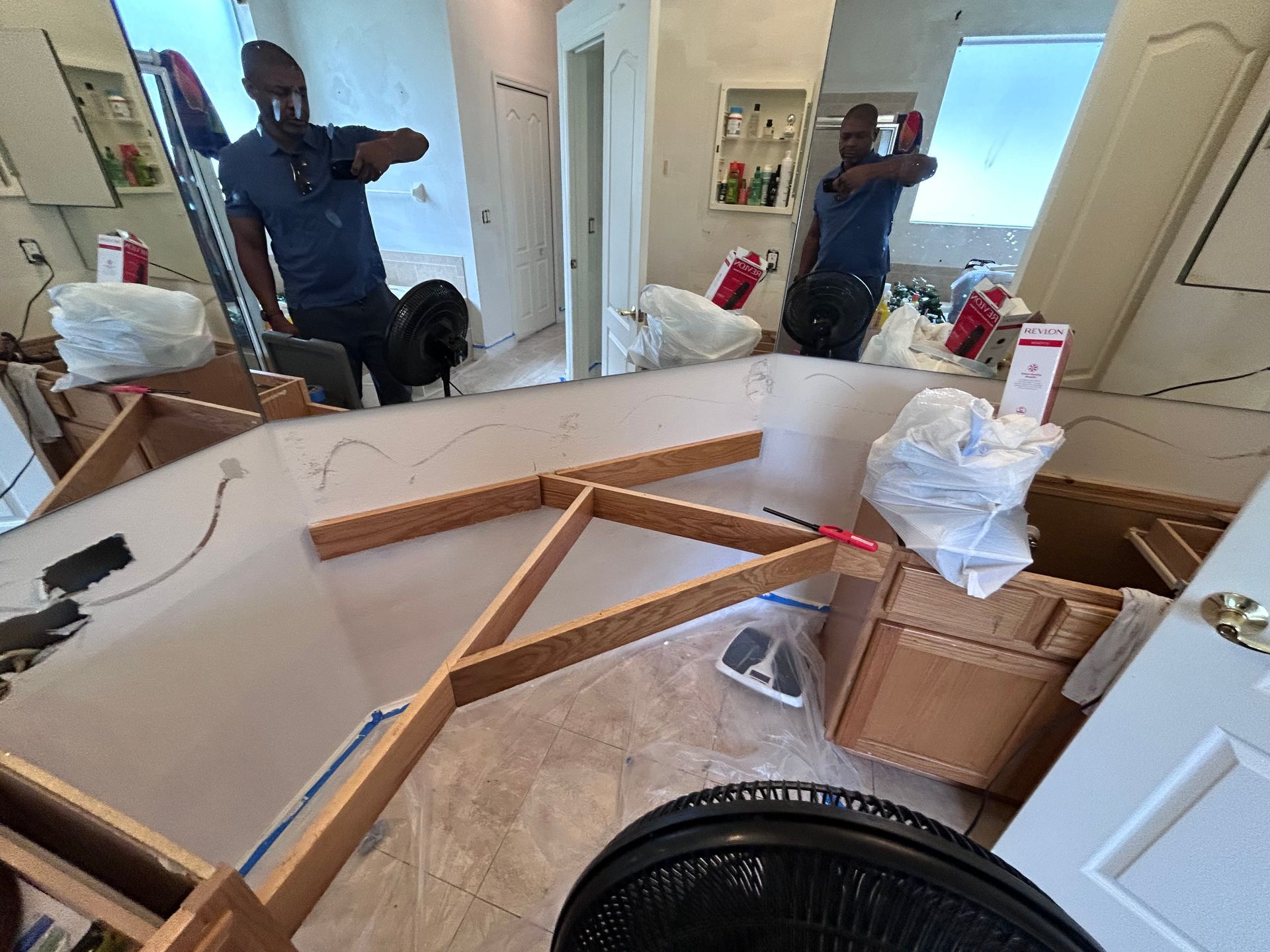 Man in a blue shirt points, surrounded by construction materials, mirrors reflect a similar scene, indoor setting.