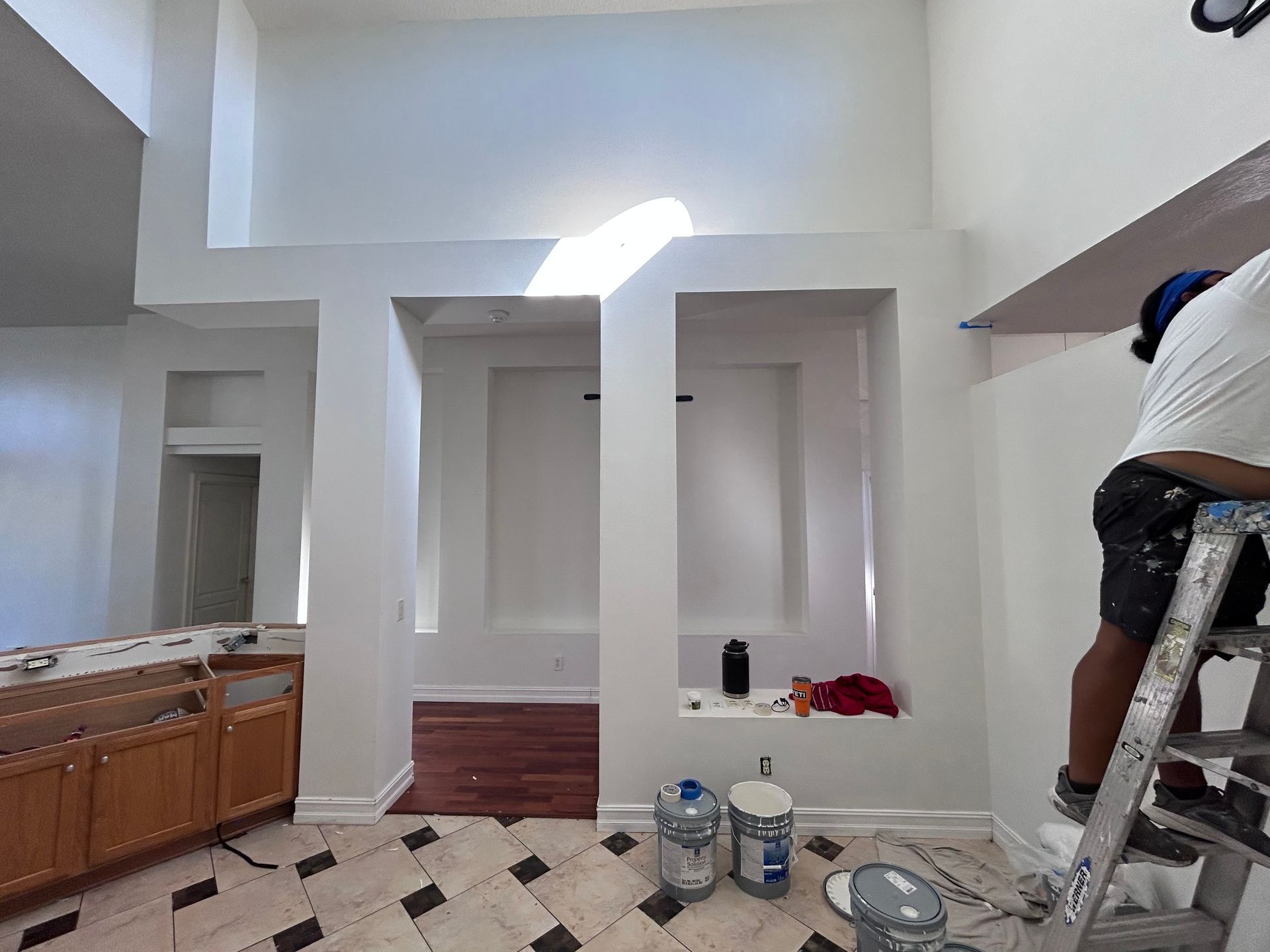 Person painting white walls in a house with recessed alcoves and a wood floor.