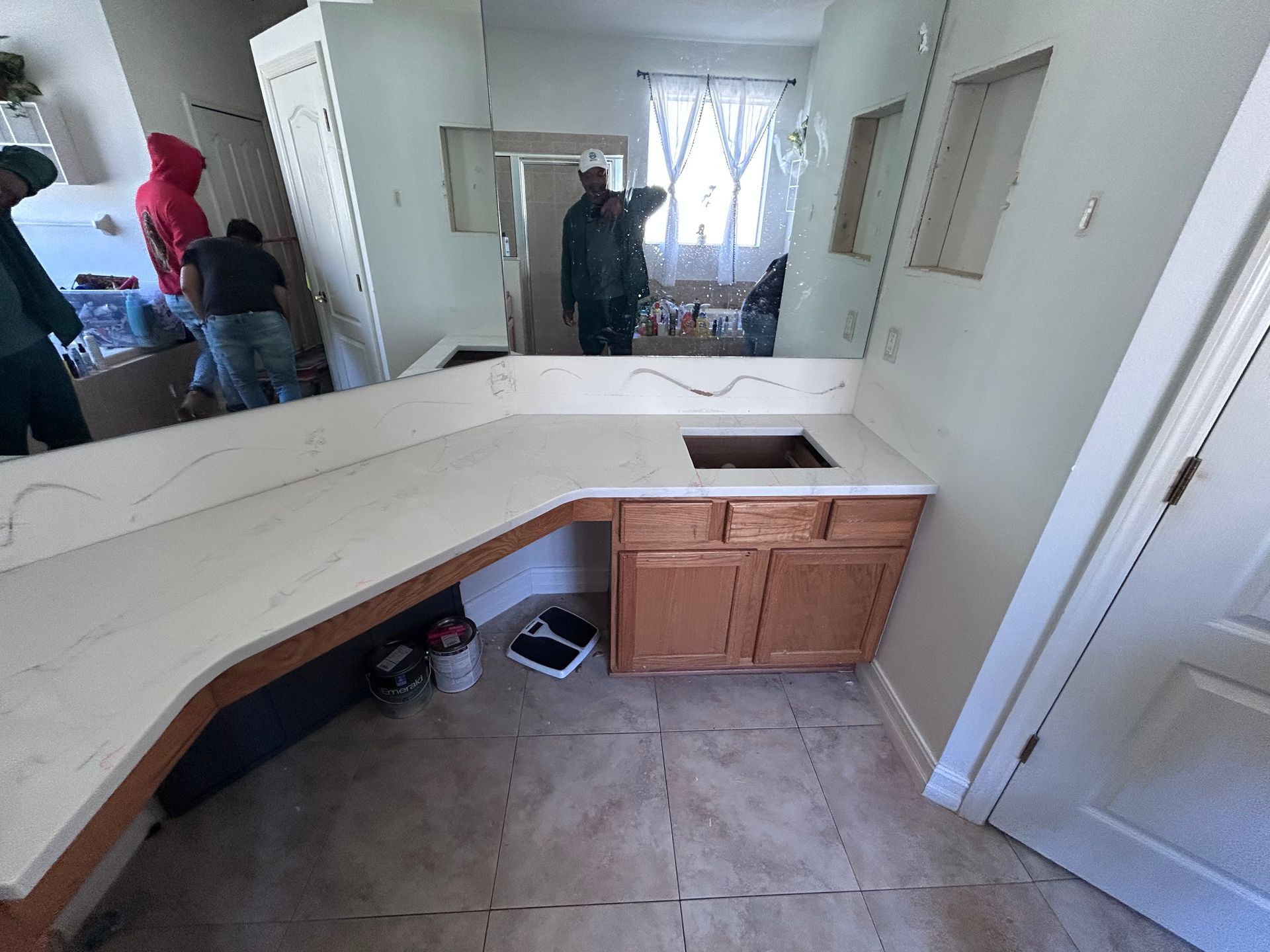 Bathroom with new white countertop and tan cabinets. People working in the background.