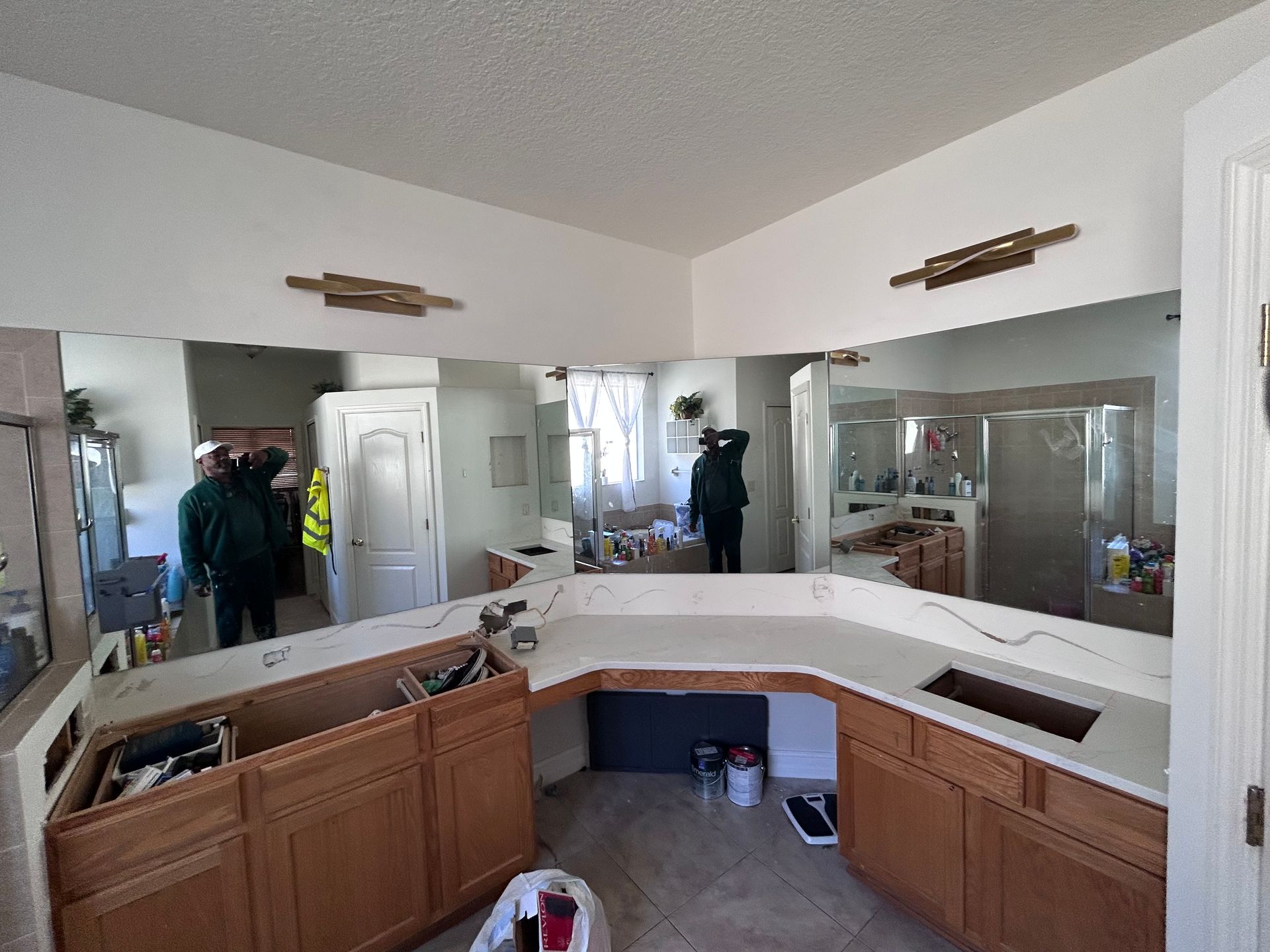 Bathroom with wooden cabinets, countertop, and large mirrors. Several people are visible.