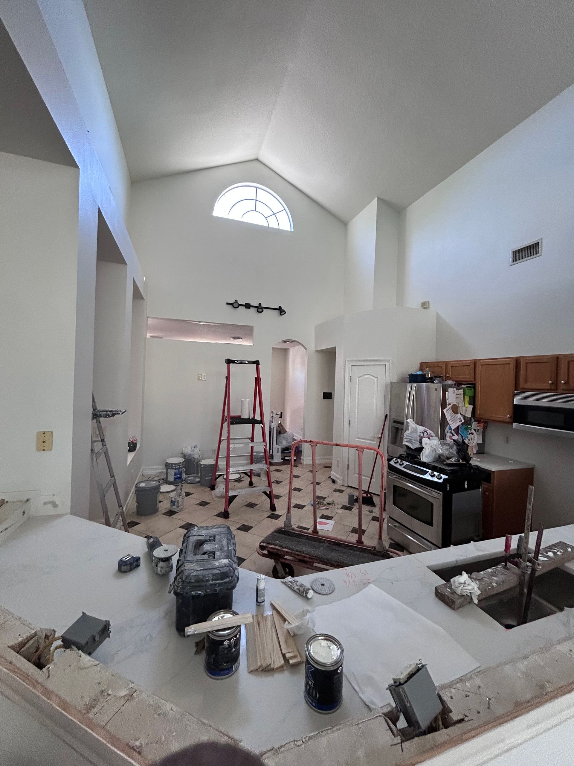 Kitchen under renovation, with tools, paint, and exposed countertops. High ceiling, arched window.