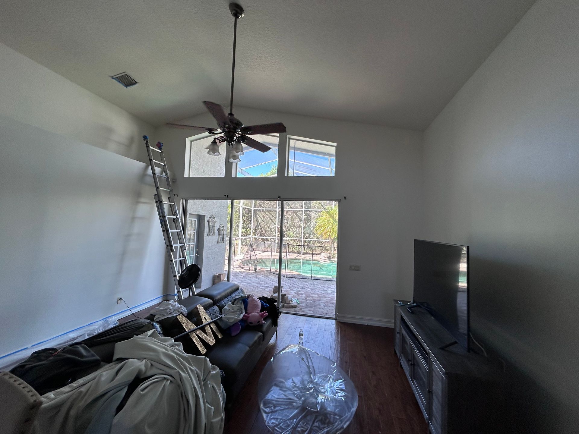 Living room with high ceiling, sliding glass door, TV on stand, ladder against wall.