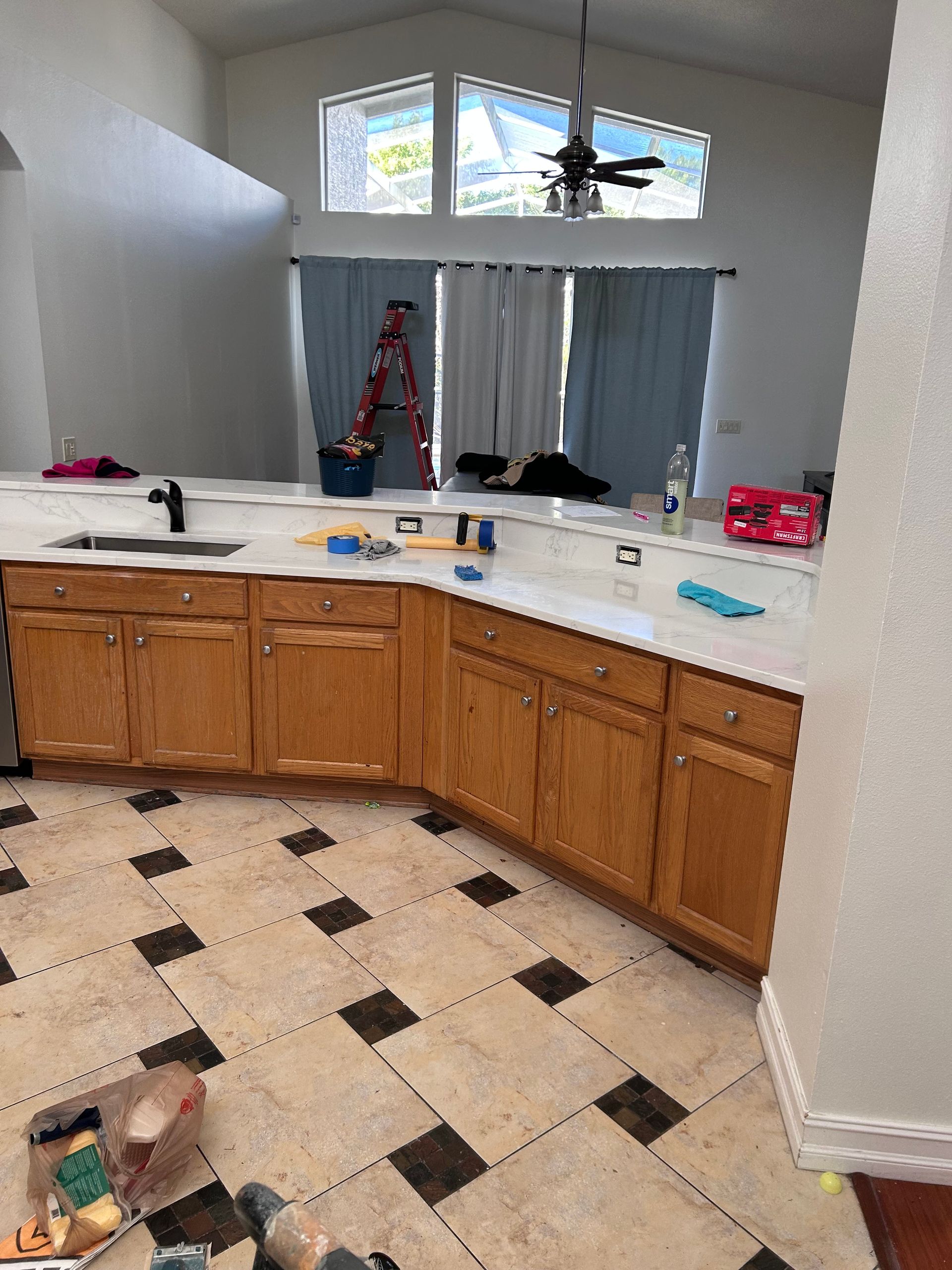 Kitchen with light wood cabinets, granite countertop, tile floor. Window with curtains and ladder.