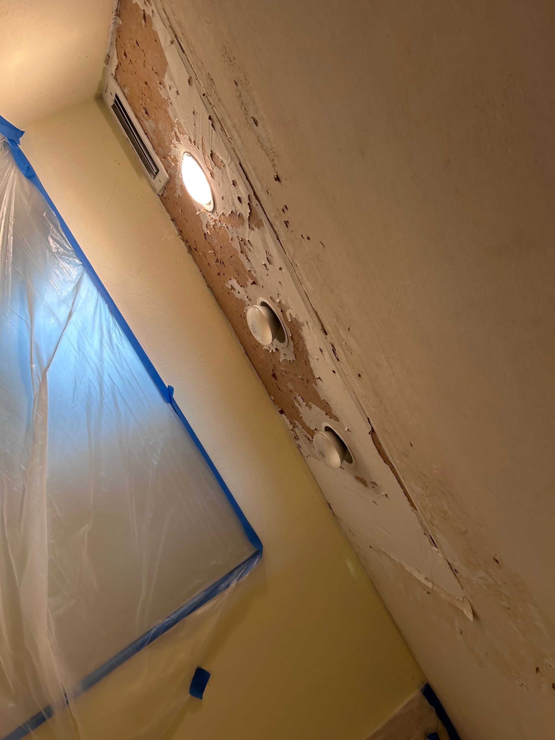 Ceiling damage with three light fixtures and vent; plastic sheeting taped on a wall.