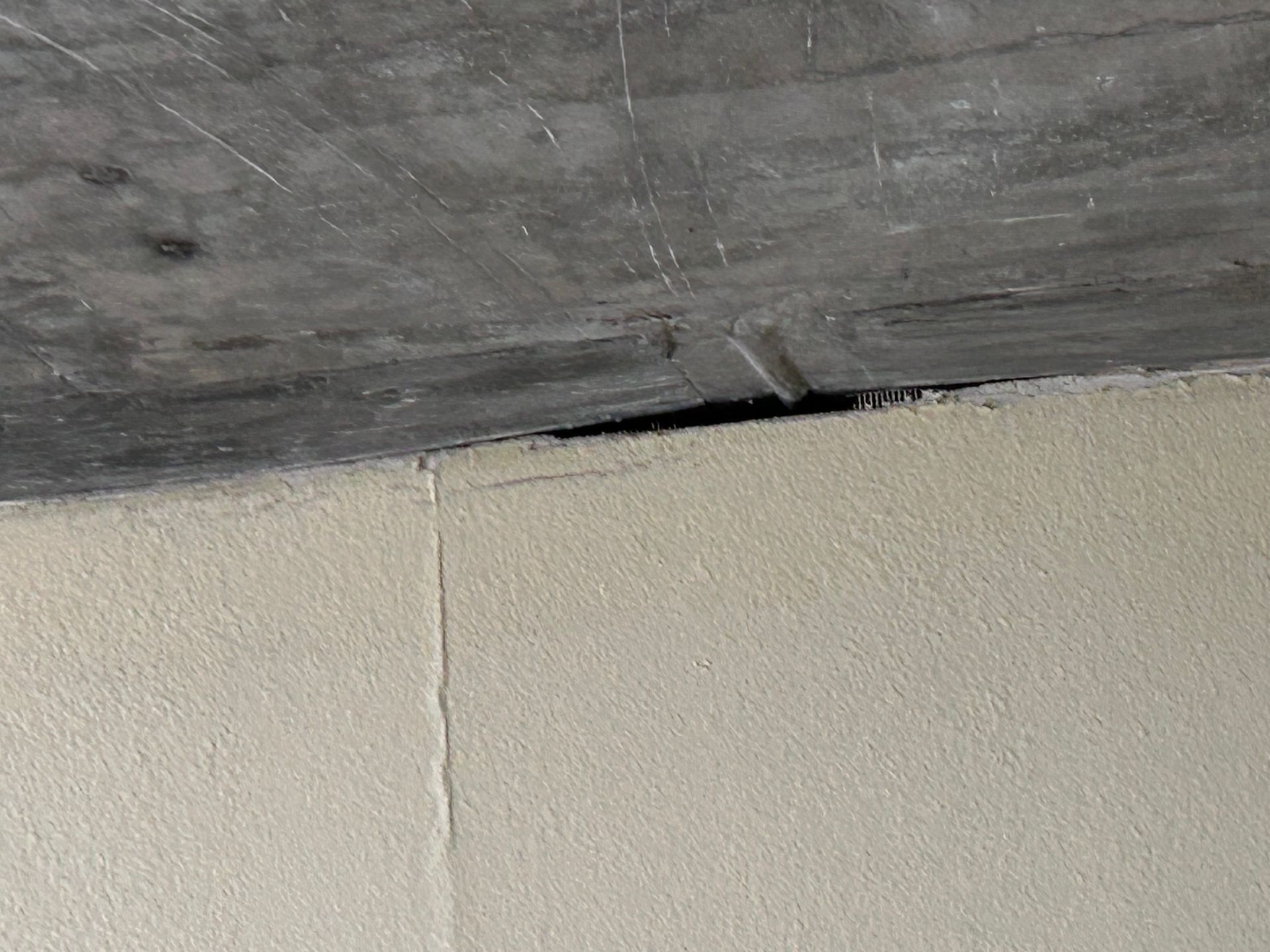 Gap between a gray concrete ceiling and a light tan stucco wall.