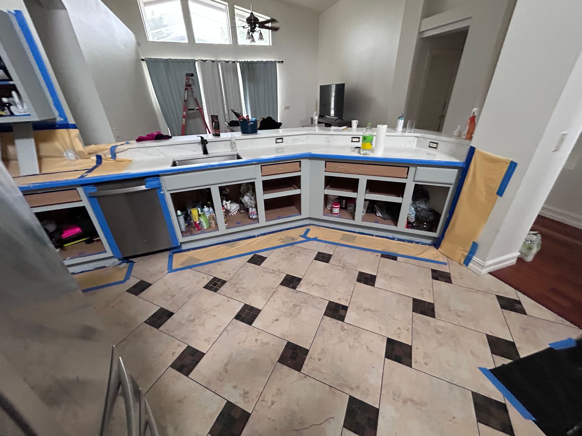 Kitchen renovation: Cabinets being painted gray, protected with blue tape. Flooring is patterned tile.